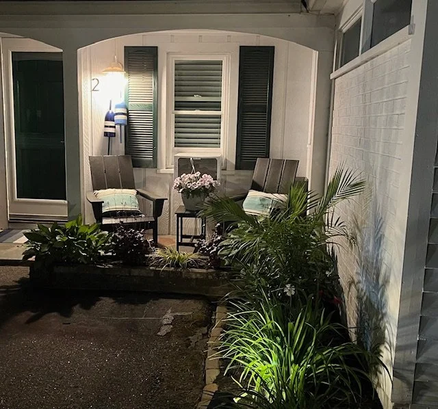 Front porch with two chairs, a small table with flowers, and outdoor plants at night.