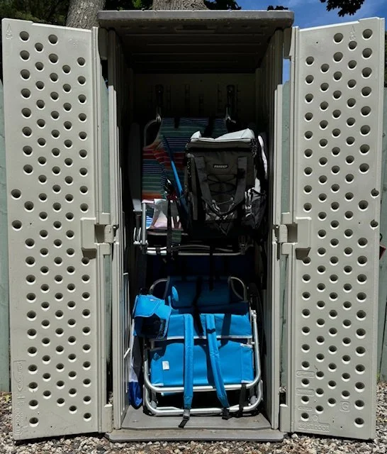 Open outdoor storage cabinet containing folded chairs, a backpack, and other outdoor gear.