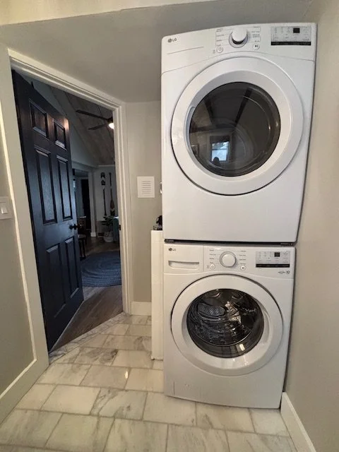 Stacked LG washer and dryer in a laundry area with gray walls and tiled floor.