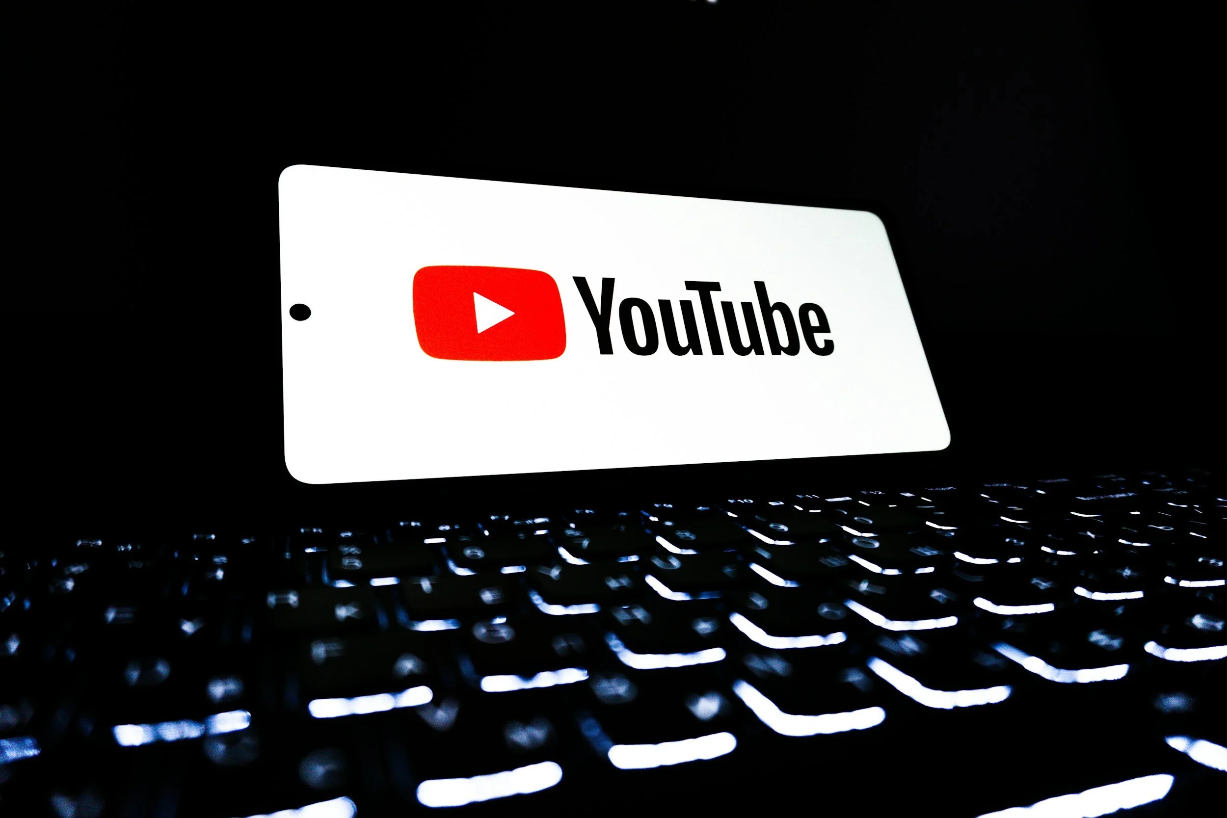 Smartphone displaying the YouTube logo on a dark background with a illuminated keyboard below.