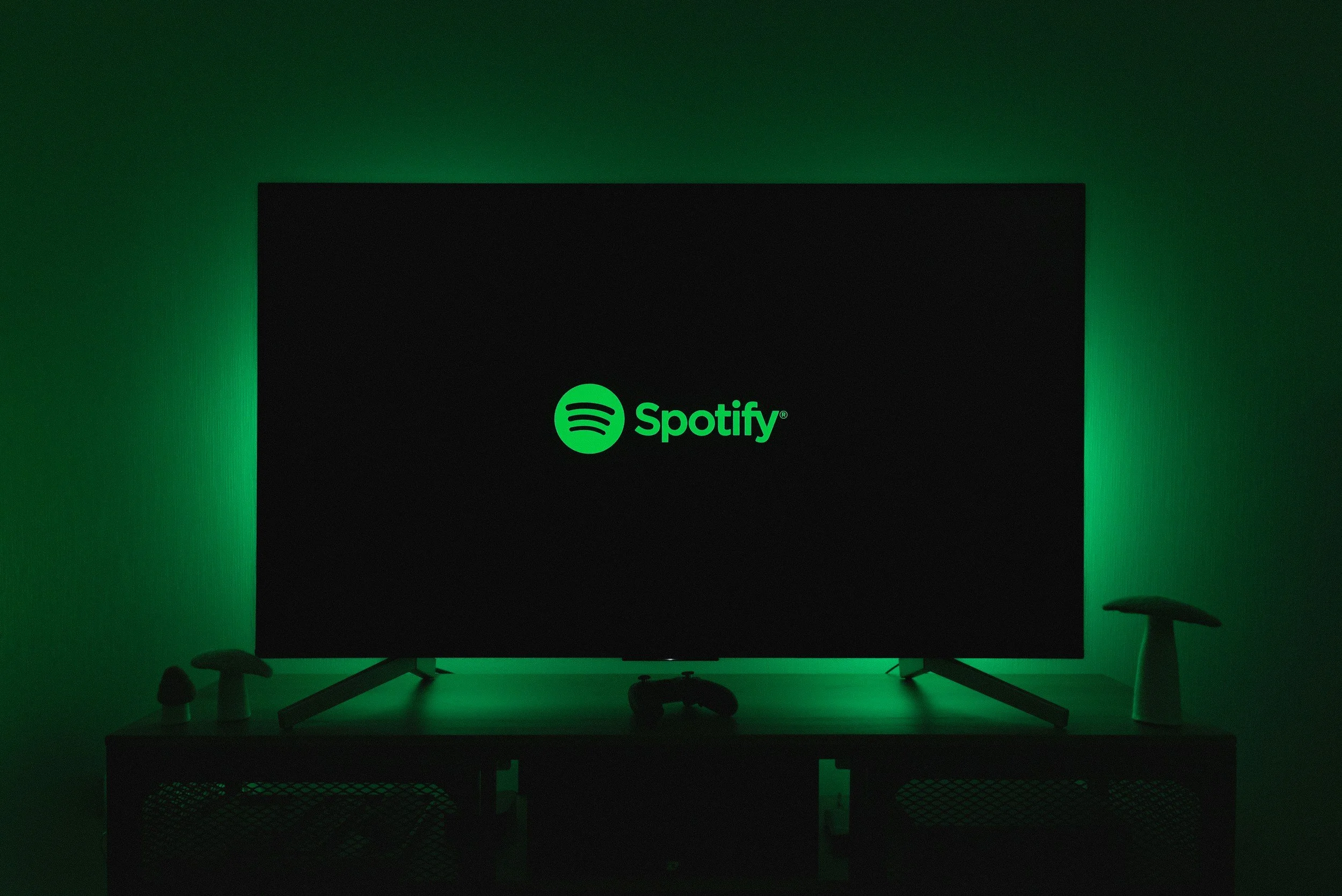 Television displaying the Spotify logo in a dark room with green backlighting