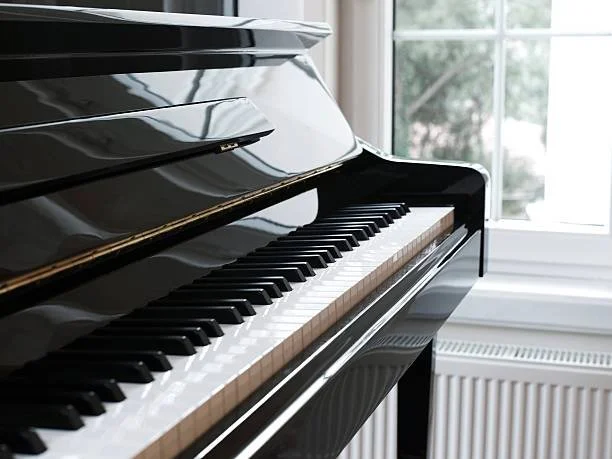 Close-up of a black grand piano keyboard near a window.