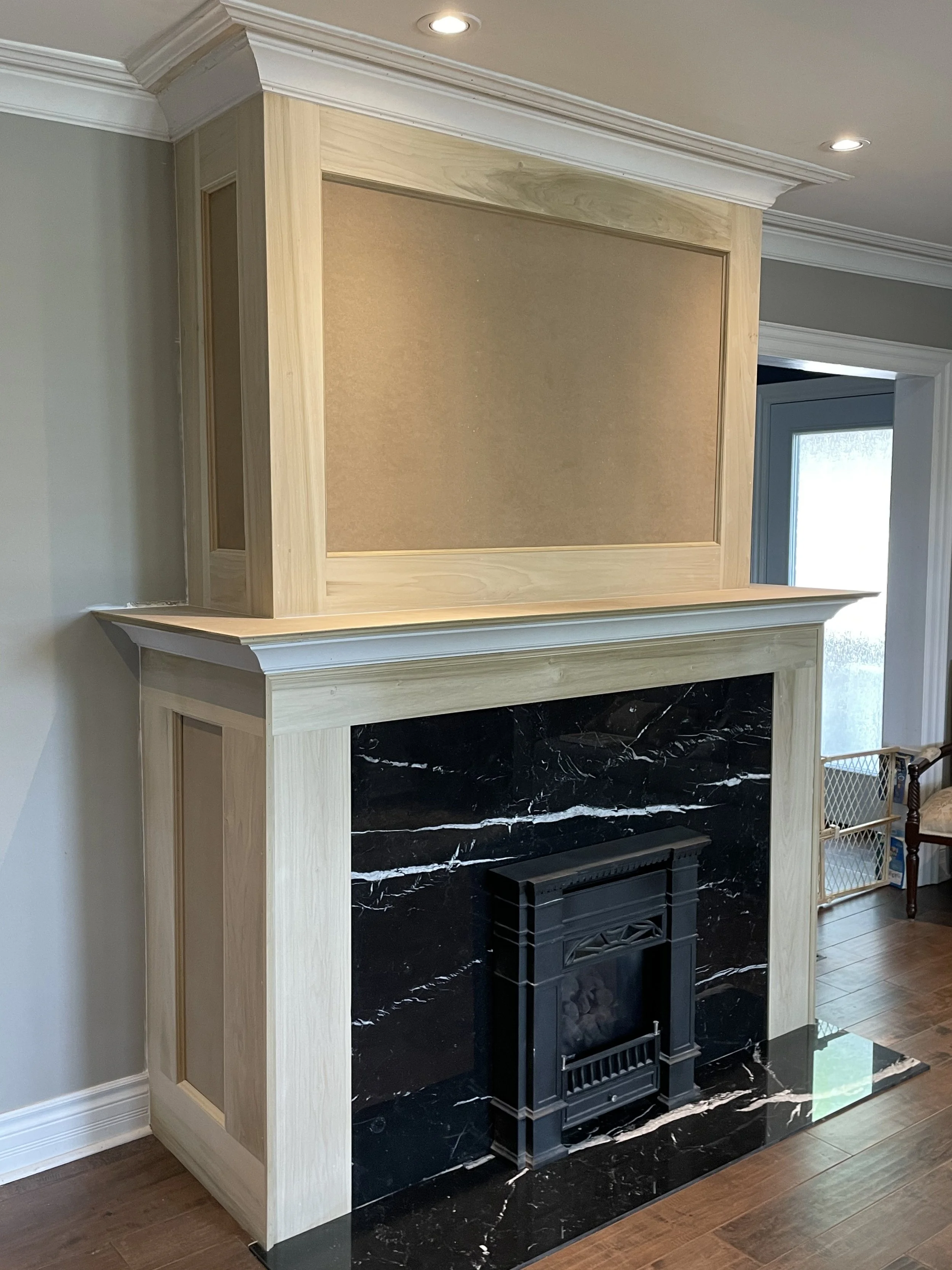 Burnt black marble fireplace with black metal insert, wooden mantel, and a beige upper panel with light wood trim in a living room.