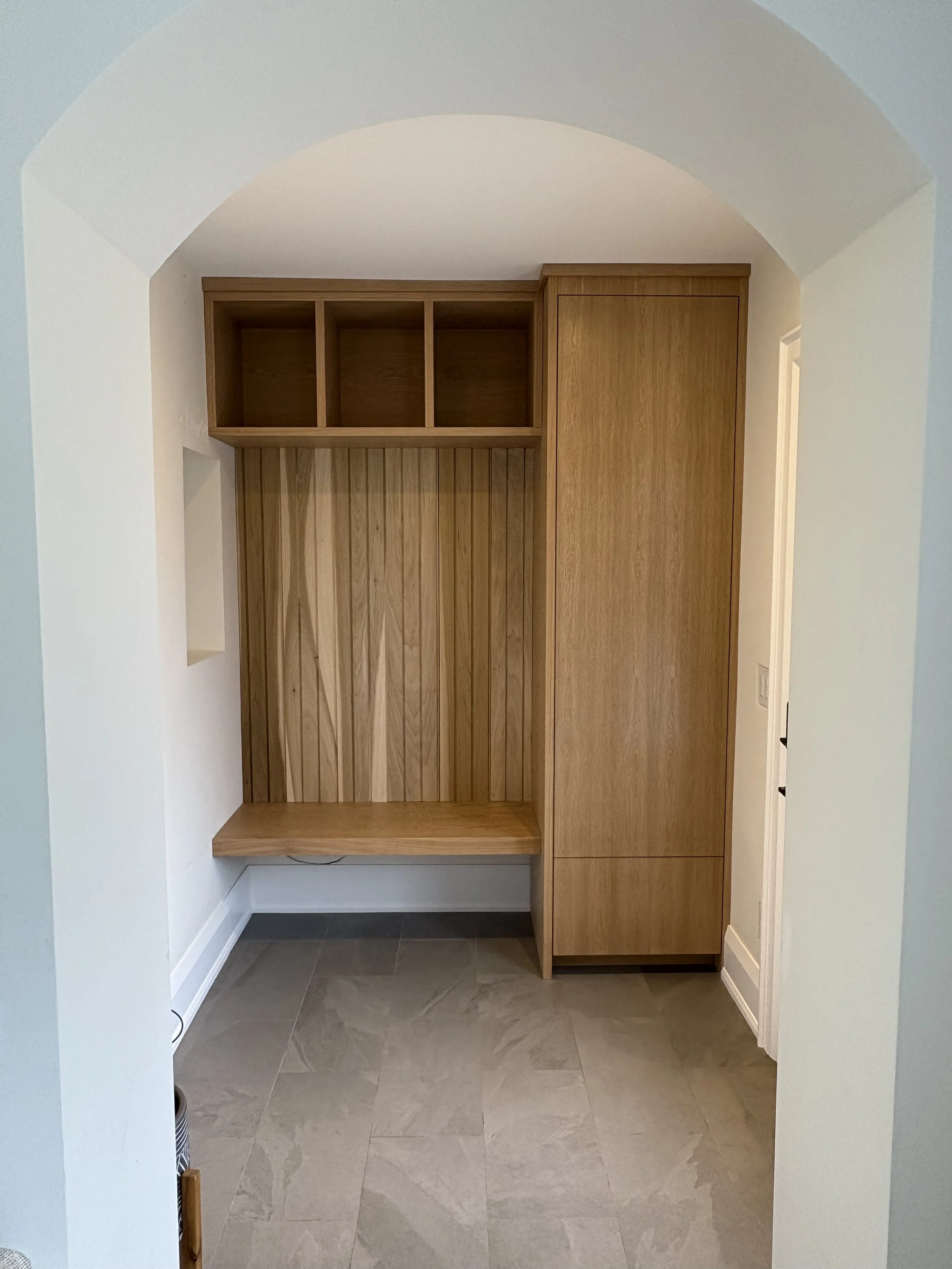Empty wooden closet with cubby shelves and a bench, within an arched entryway.