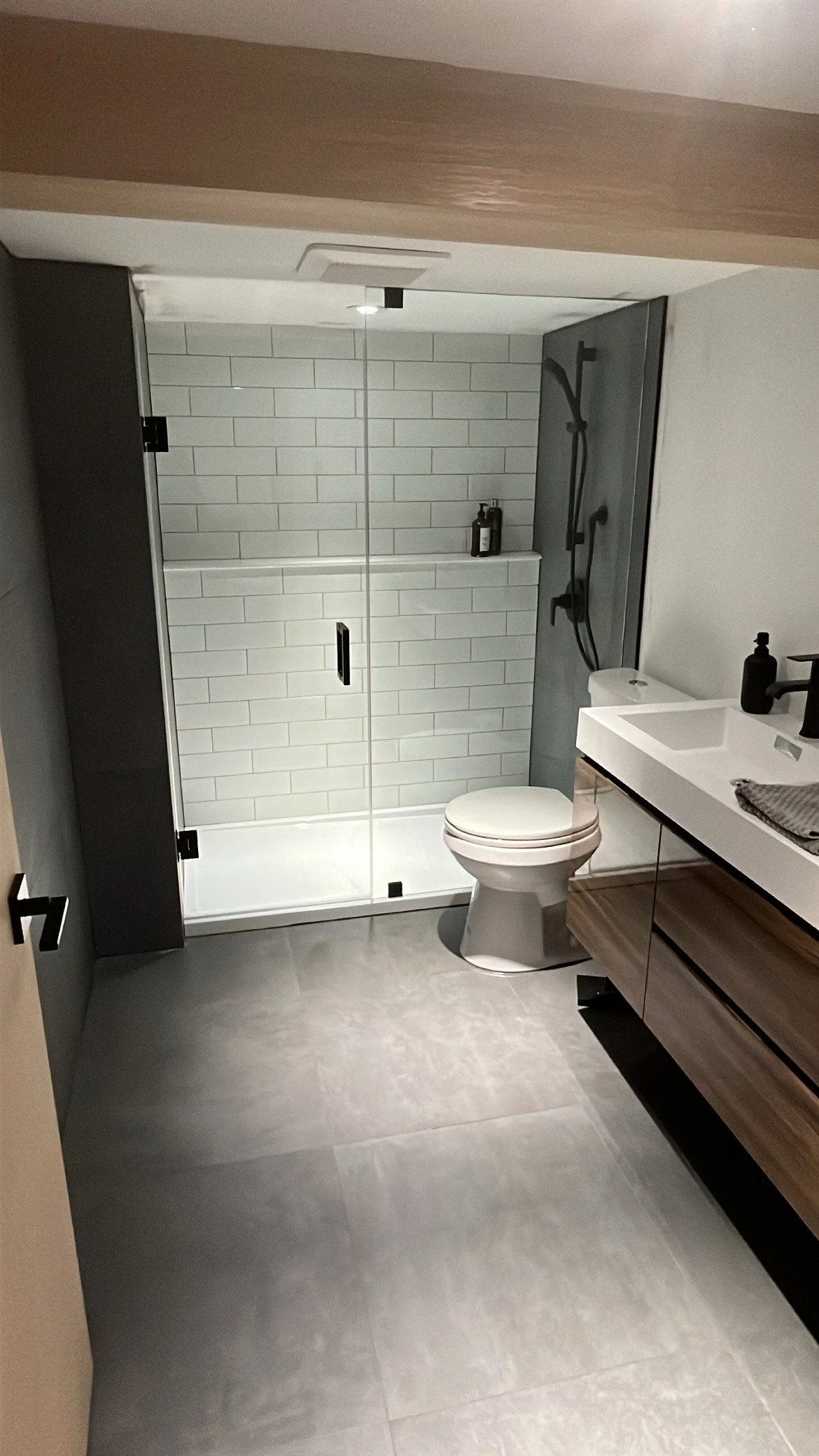 Modern bathroom with glass-enclosed shower, white tiled walls, white toilet, and a floating vanity with a rectangular sink and black fixtures.