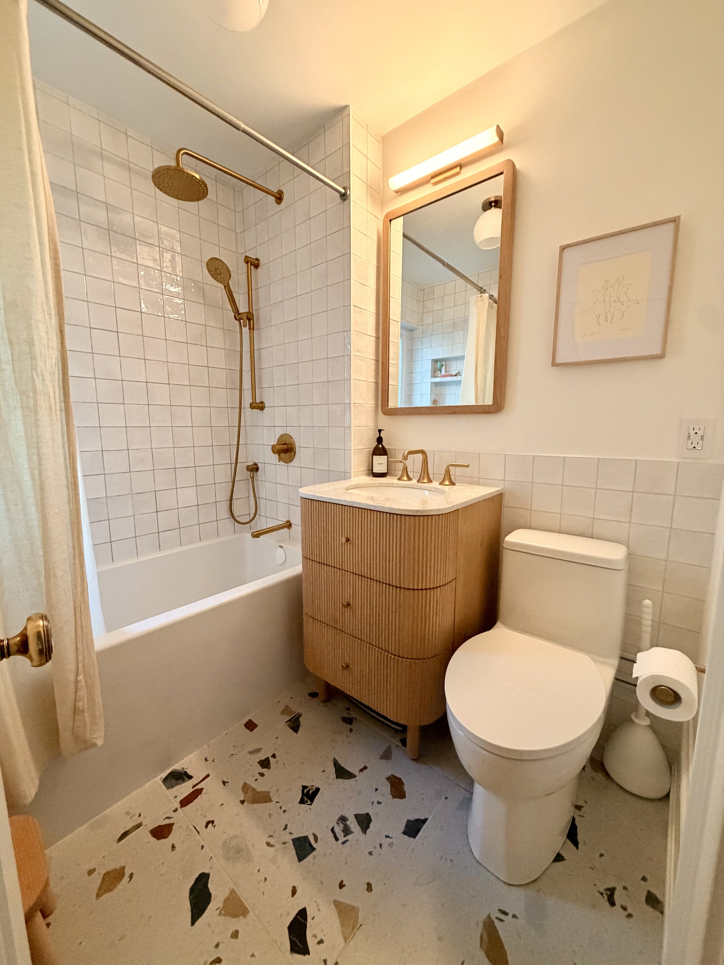 A modern bathroom vanity with a white countertop, two sinks, and threecentred mirrors. Wooden cabinets with black handles, and a round bathtub partially visible in the foreground.