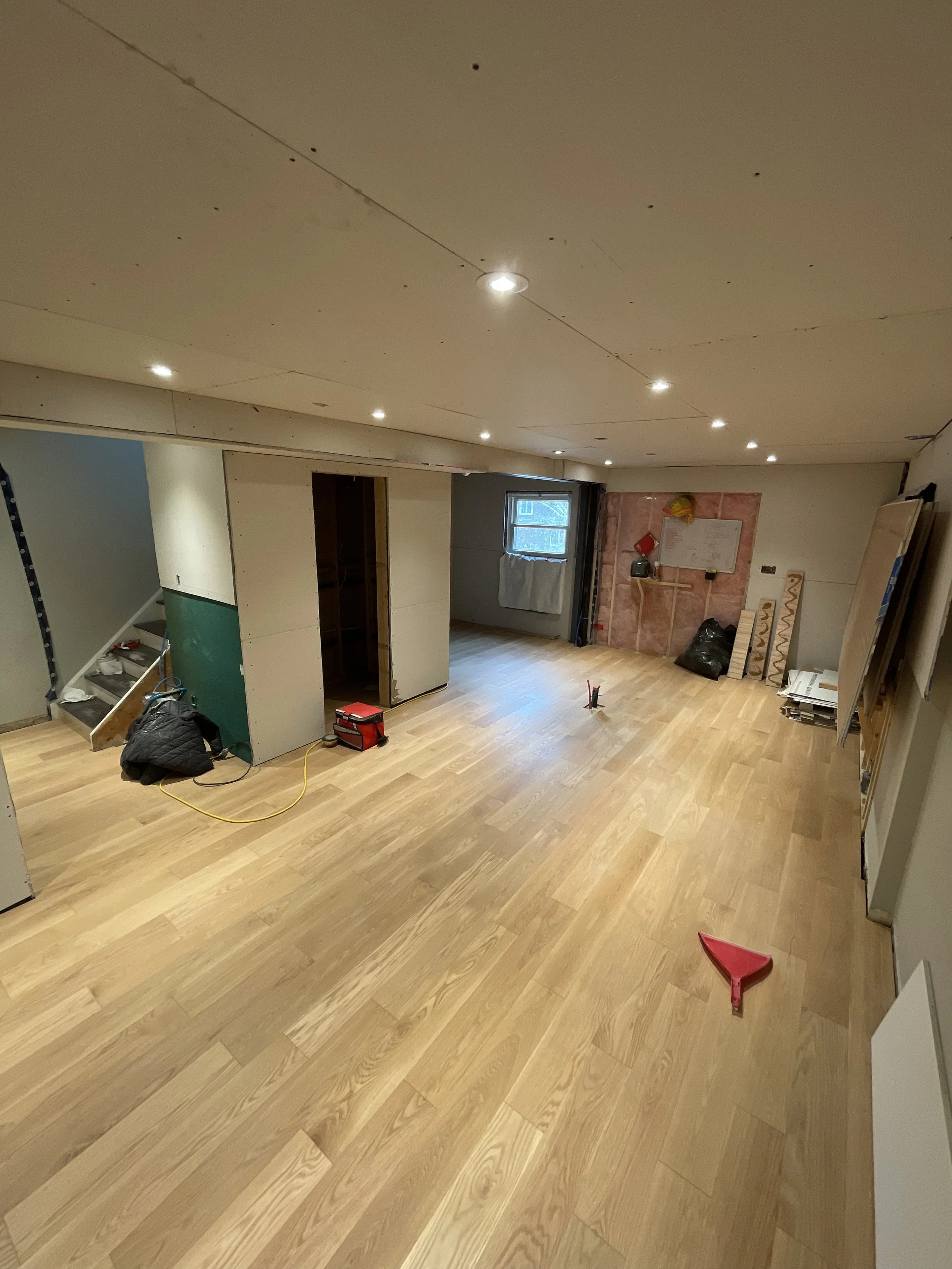 A room under construction with wooden flooring, partially finished walls, and construction tools and materials scattered around.
