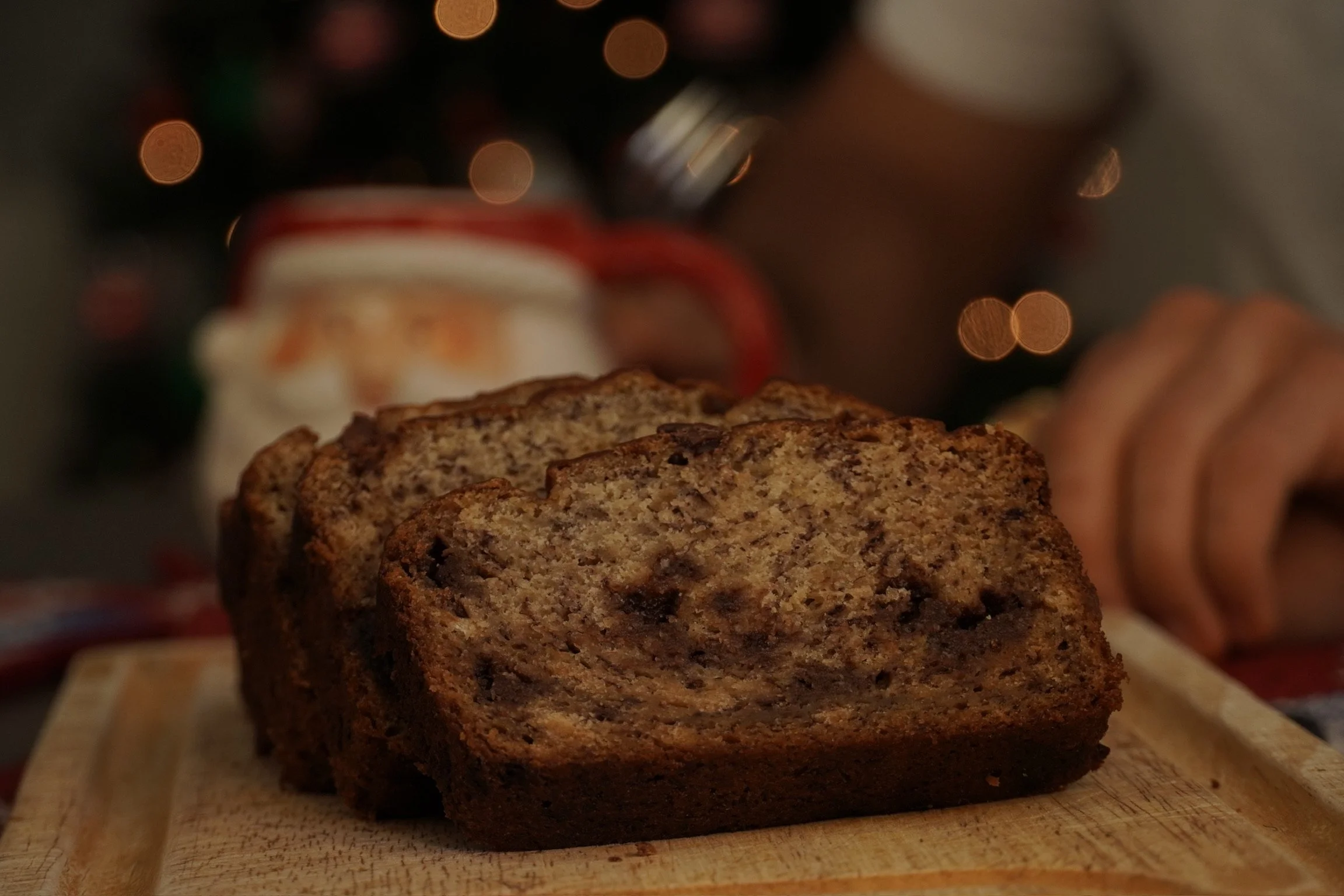 A loaf of marble banana bread on a wooden cutting board with a blurred background including a Christmas mug and ornaments.