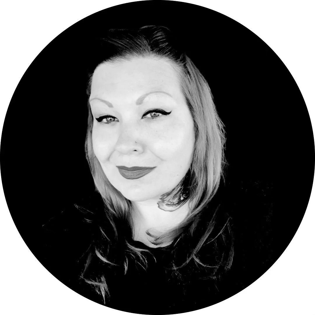 Black and white portrait of Nicole Stover with light-colored hair, makeup, and lipstick, smiling slightly against a dark background.