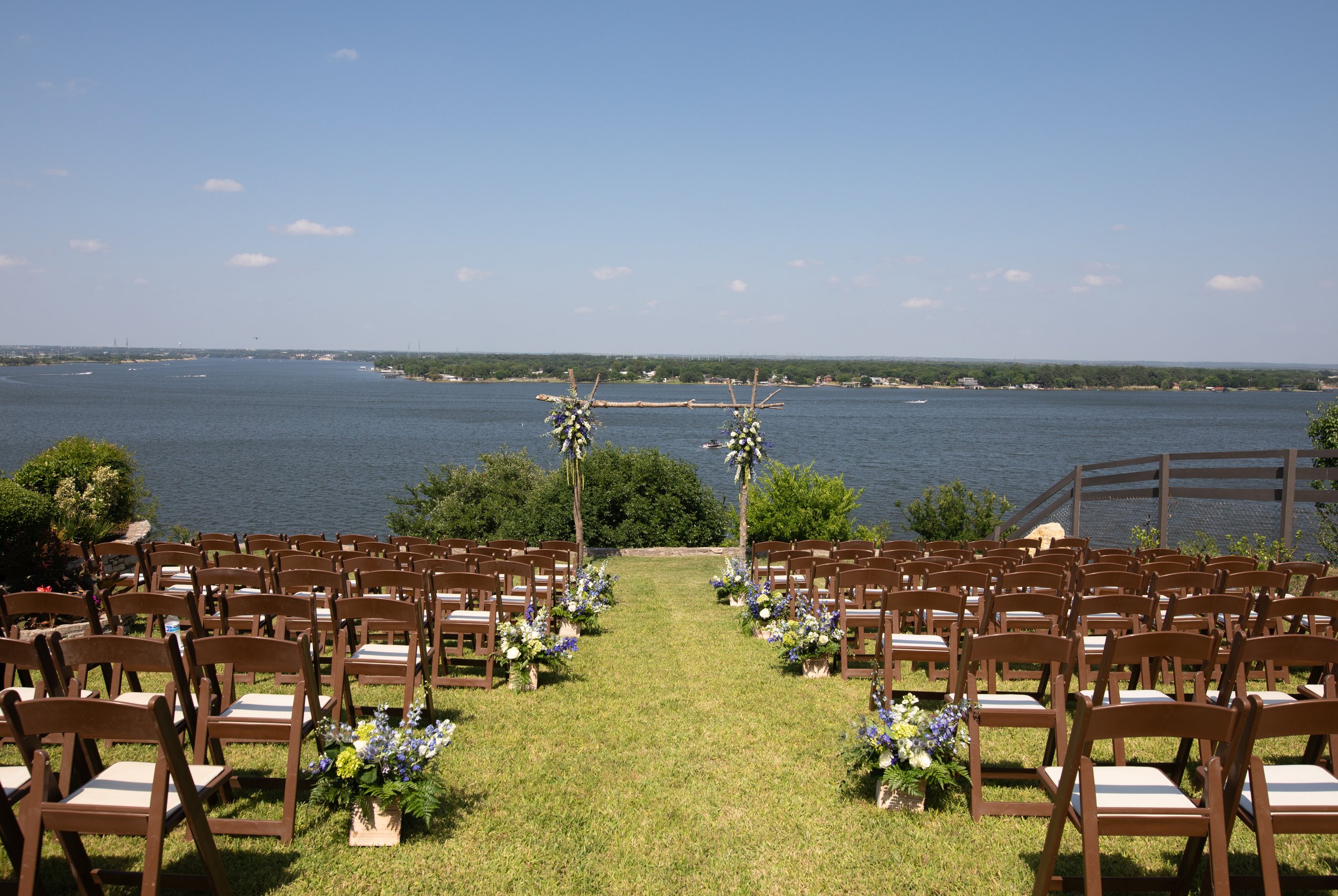Outdoor wedding setup by a lake with rows of chairs, floral decorations, and a wooden arch