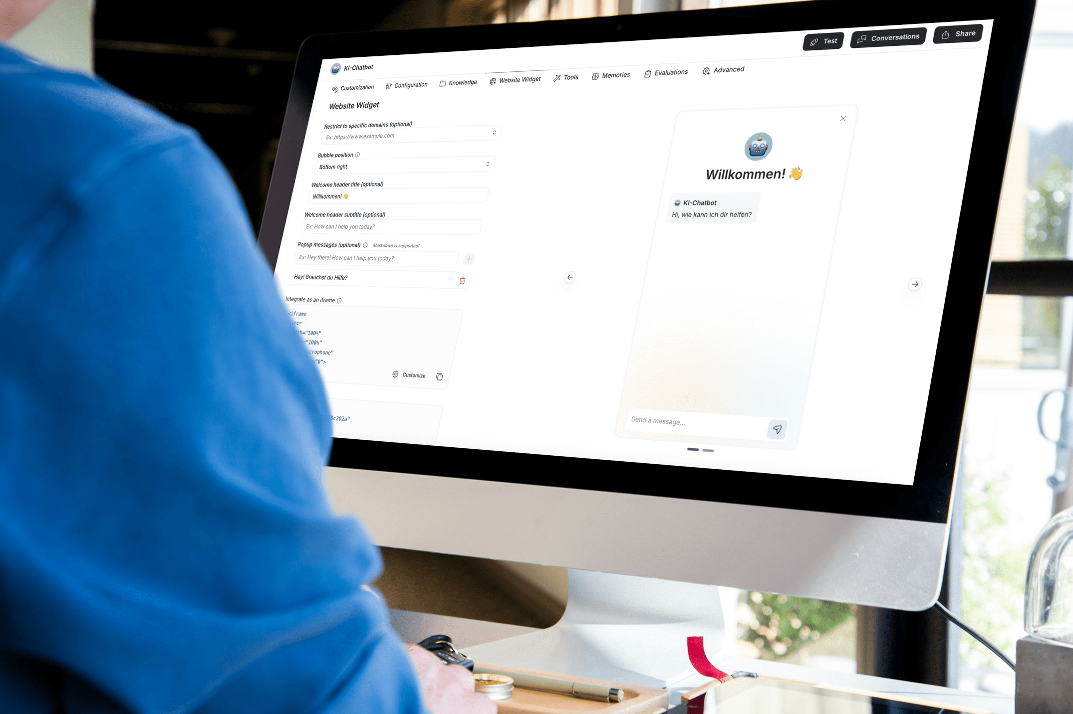 Ein Computerbildschirm zeigt eine Chatbot-Konfigurationsseite mit der Begrüßungsnachricht 'Willkommen! 👋' und einem Chat-Fenster mit einem freundlichen Roboter-Icon, der auf Deutsch antwortet.