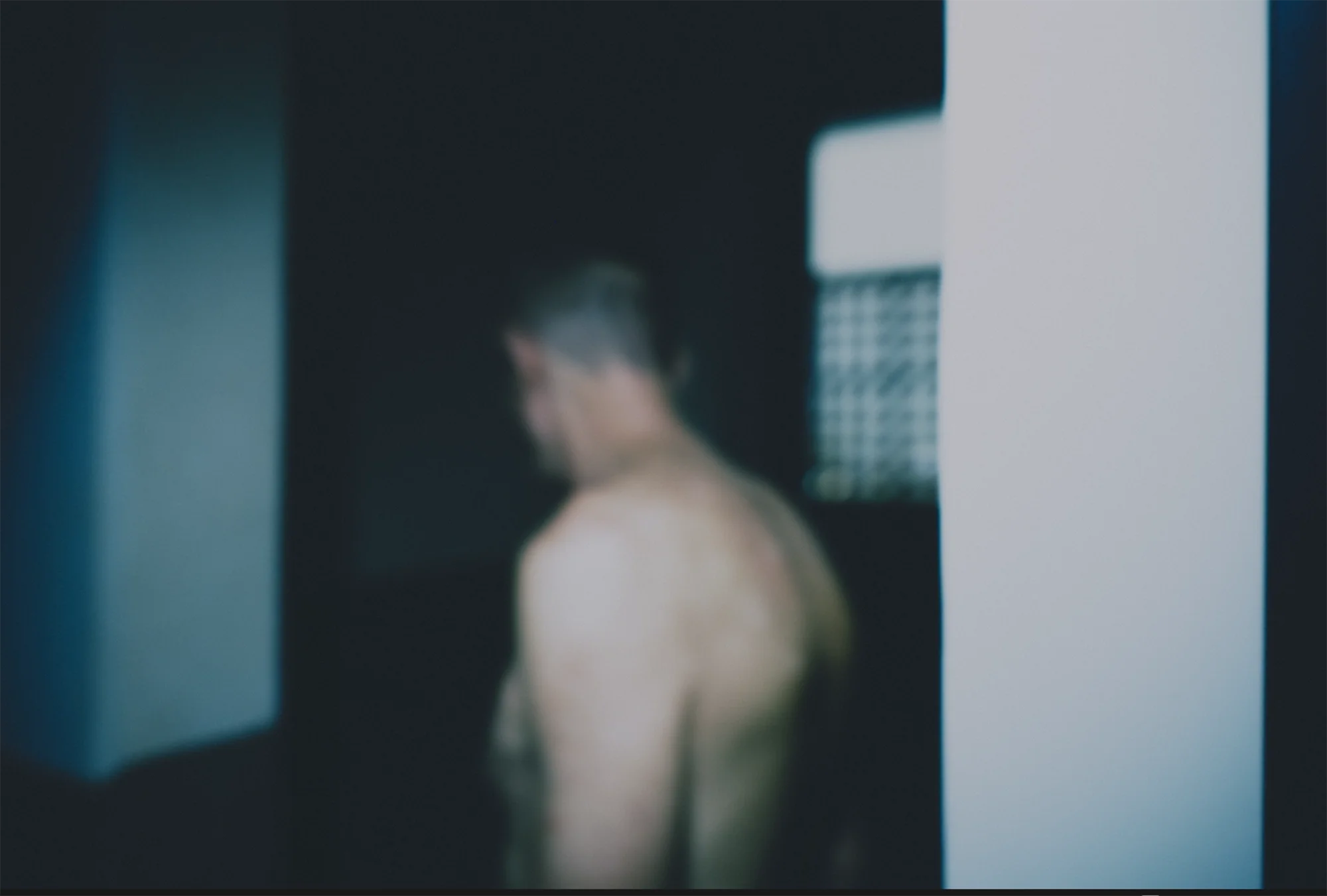 Une personne torse nu vue de dos dans un environnement sombre avec des lumières blanches et bleues.