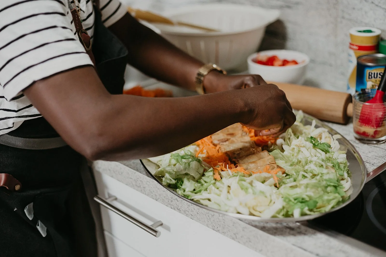 Person preparing a salad with shredded lettuce and carrots in a large bowl on a kitchen counter.
