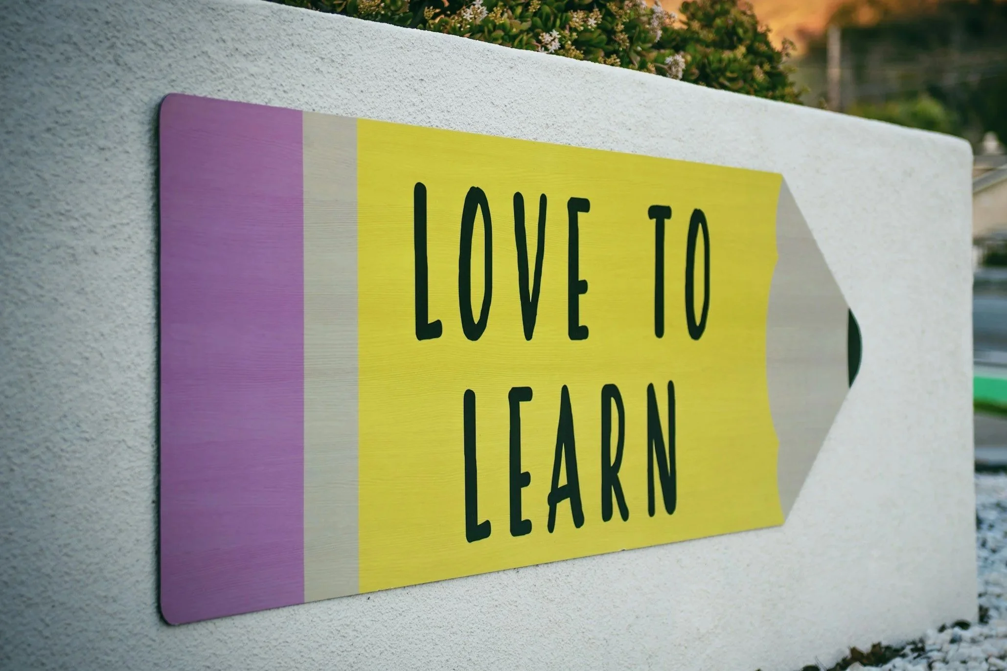 A colorful sign with yellow, purple, and white stripes that reads 'Love to Learn' mounted on a white wall.