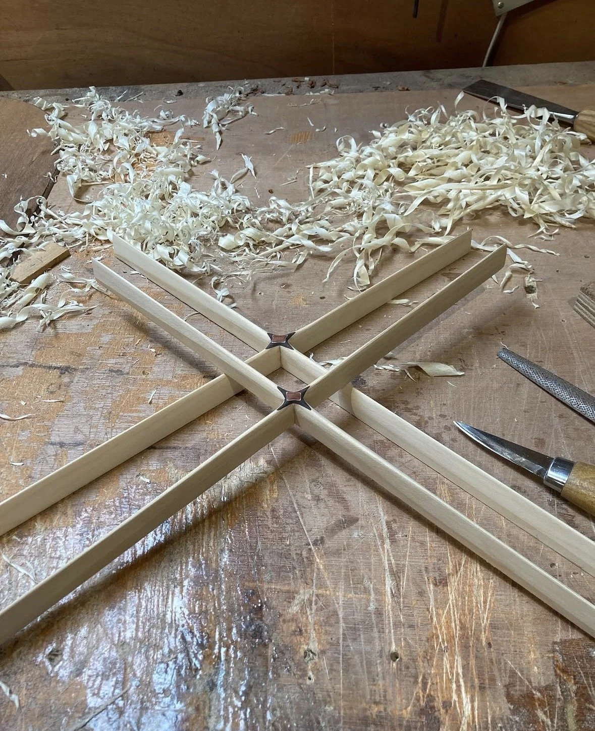 Wooden workbench with wood shavings, tools, and edges of wooden strips arranged in a star pattern for woodworking project.