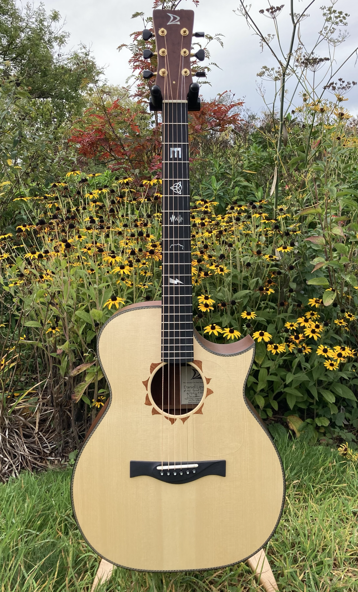 An acoustic guitar outdoors on grass, positioned in front of yellow flowers and green foliage.