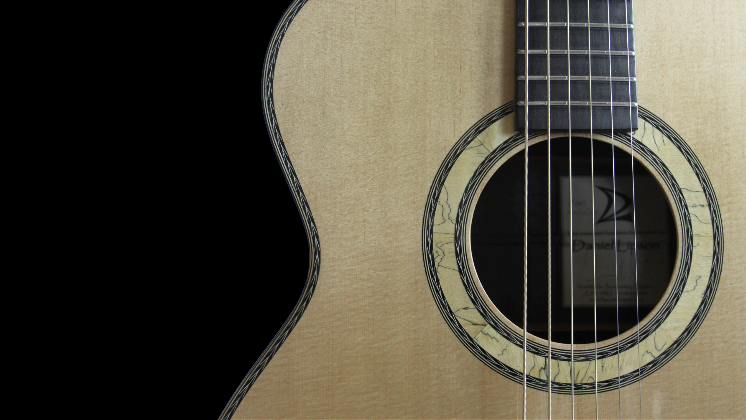 Close-up of an acoustic guitar with a light wood finish, black sound hole, and black pickguard.