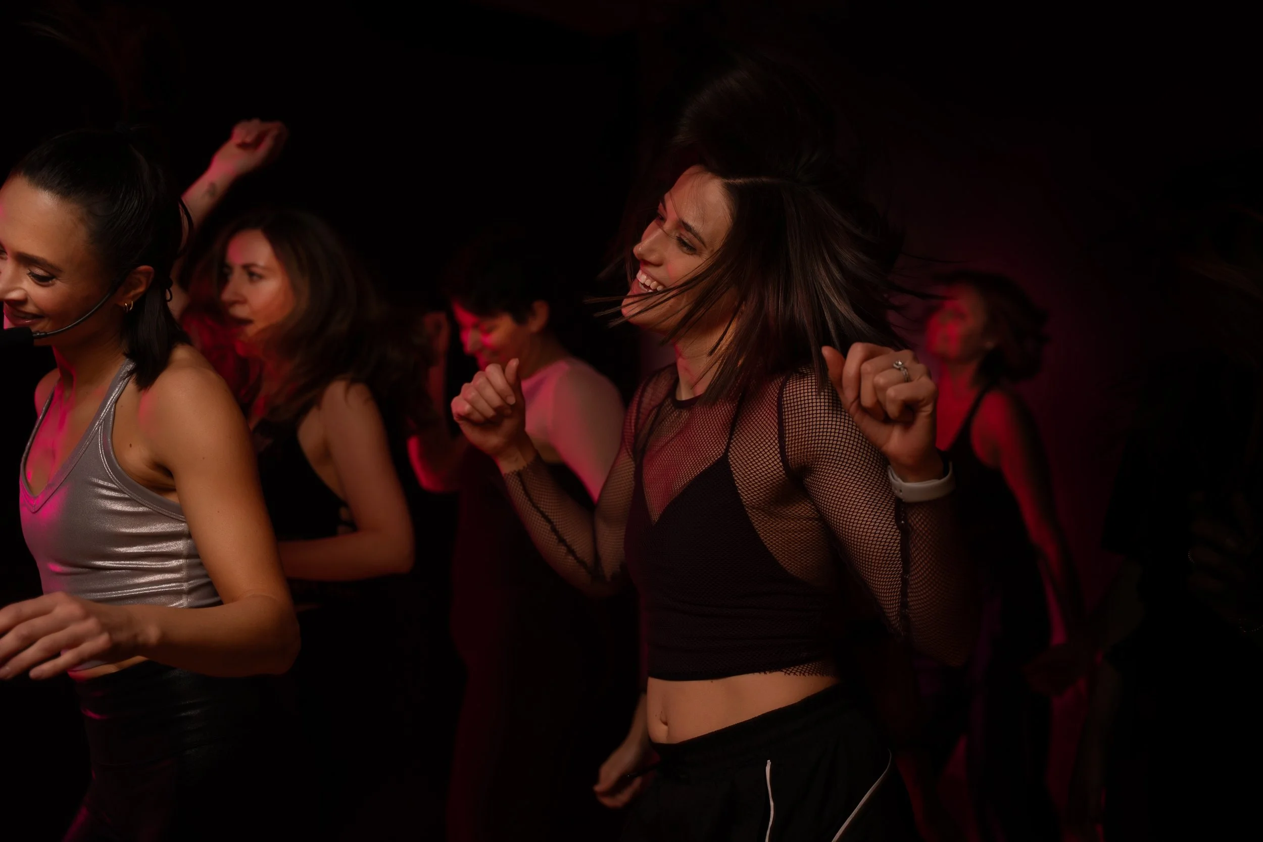 Group of women dancing together in a nightclub, smiling and enjoying the music, with colorful low lighting.