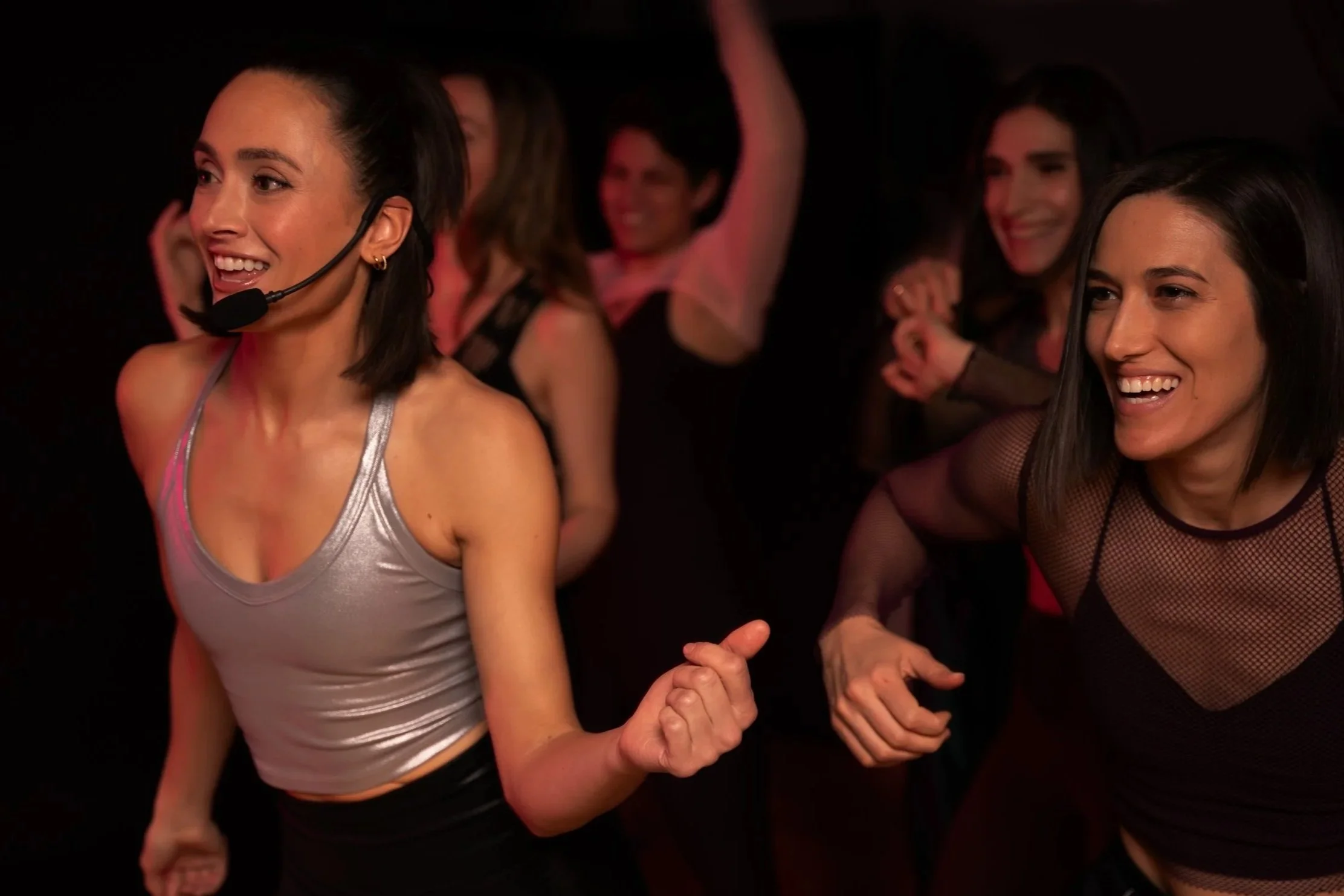 Women dancing and smiling at a party or nightclub with dark background.