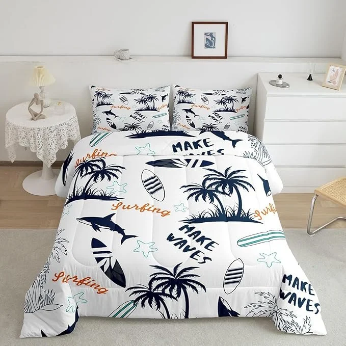 A bedroom with a white bedspread decorated with navy and orange surfing motifs, including palm trees, surfboards, and the phrases 'Make Waves' and 'Surfing.' Two matching pillowcases feature the same tropical design. The room has a white side table with a lamp and a sculpture, a white dresser with decorative items, and a framed picture hanging on the wall.