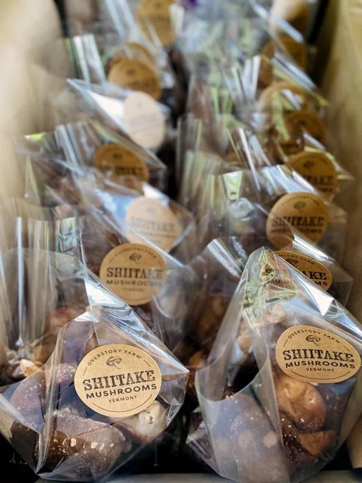Packages of Shiitake mushrooms from Upstream Farm in Vermont, wrapped in clear plastic and labeled with a round brown sticker.