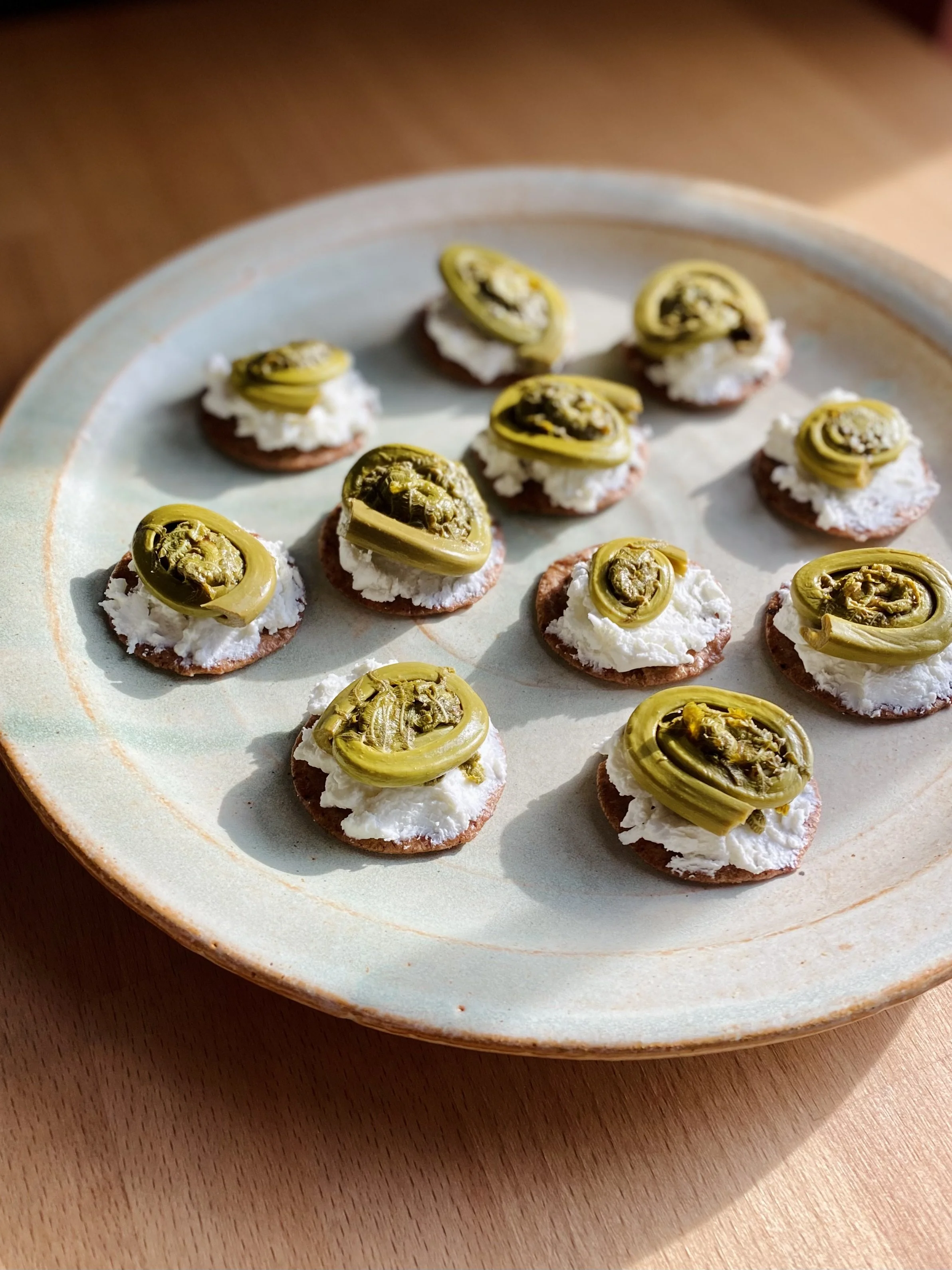 Small round crackers topped with cream cheese and sliced pickled jalapeños on a ceramic plate.