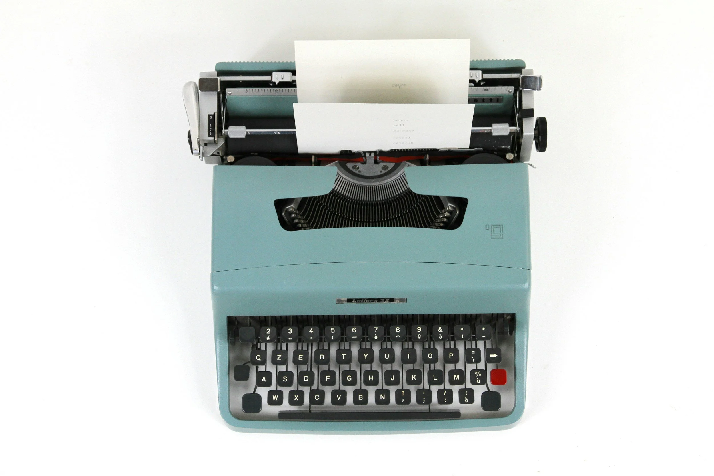 A vintage light blue typewriter with a sheet of paper inserted, viewed from above on a plain white background.