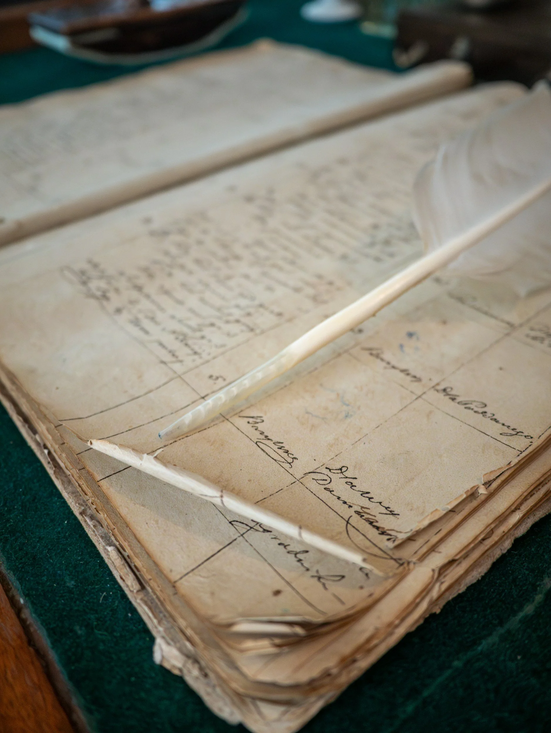 Close-up of an old, weathered ledger book with handwritten entries, a quill pen resting on the pages, used for writing or recording information.