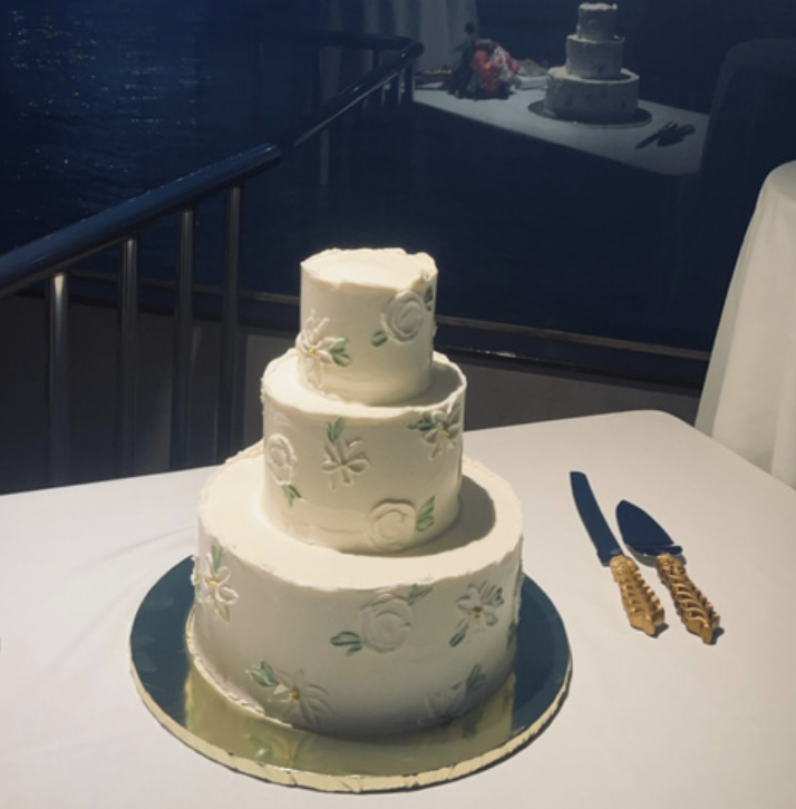 Three-tiered white wedding cake with floral decorations on a table with a cake knife and server.