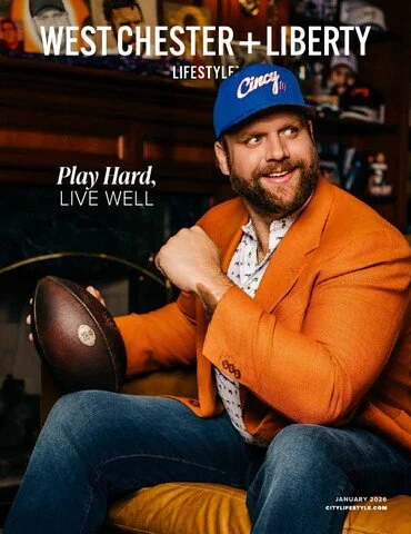 A man wearing a blue Cincinnati cap and an orange blazer sitting on a yellow chair, holding an American football, with text promoting West Chester and Liberty Lifestyle, January 2024.