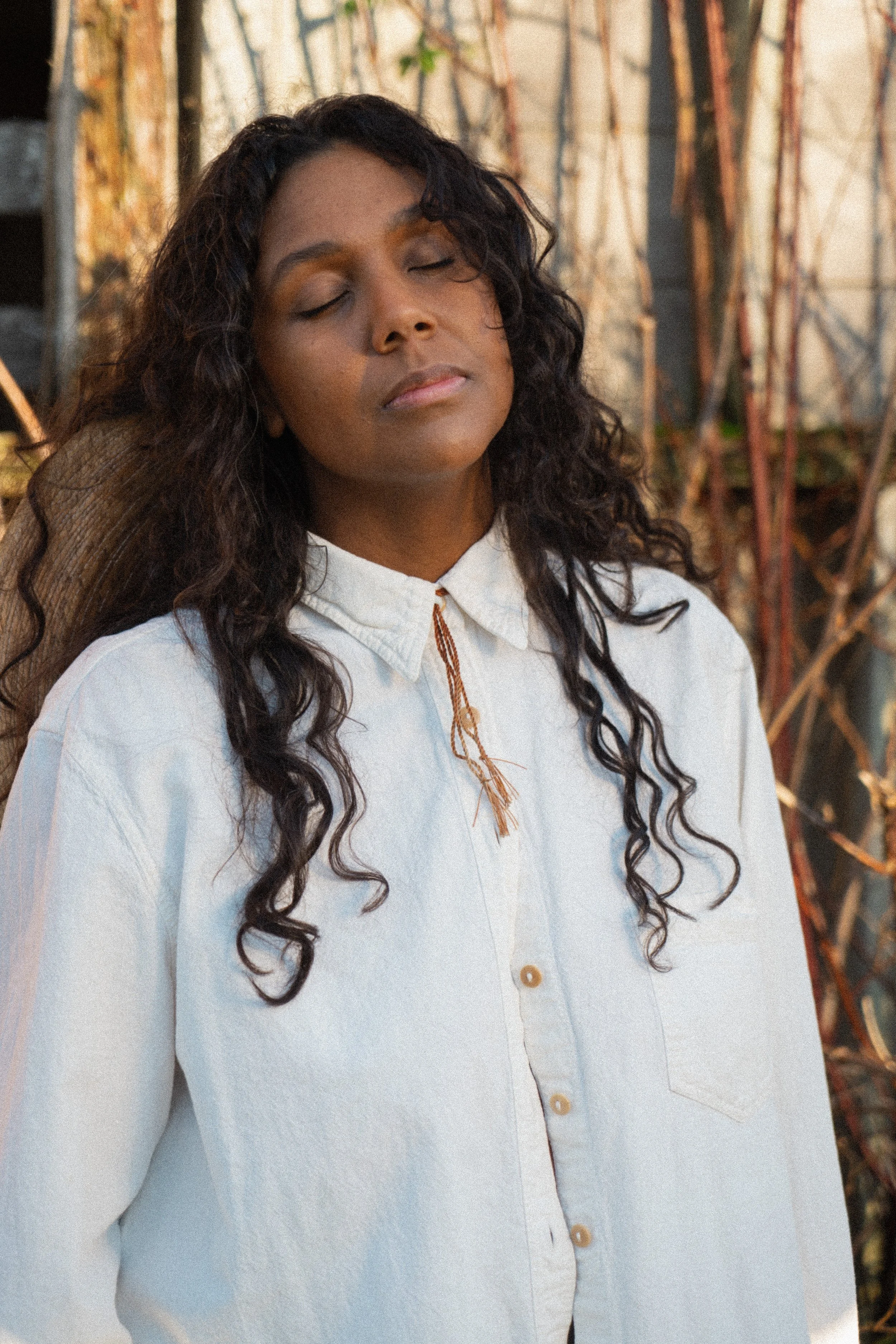 Desiree Dawson in a western creative photoshoot wearing a white blouse eyes closed taking a deep breath curly hair framing her face