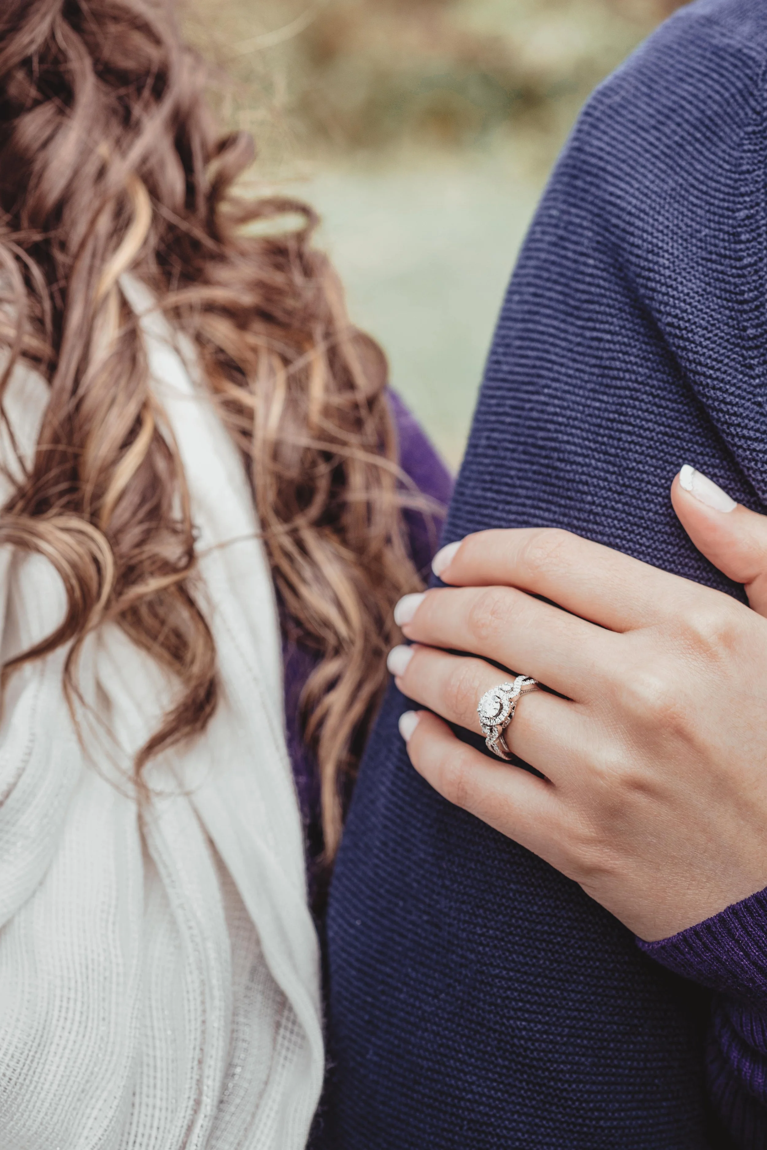 Close-up of a woman's hand resting on a man's arm, showcasing an engagement ring with a diamond and a wedding band.