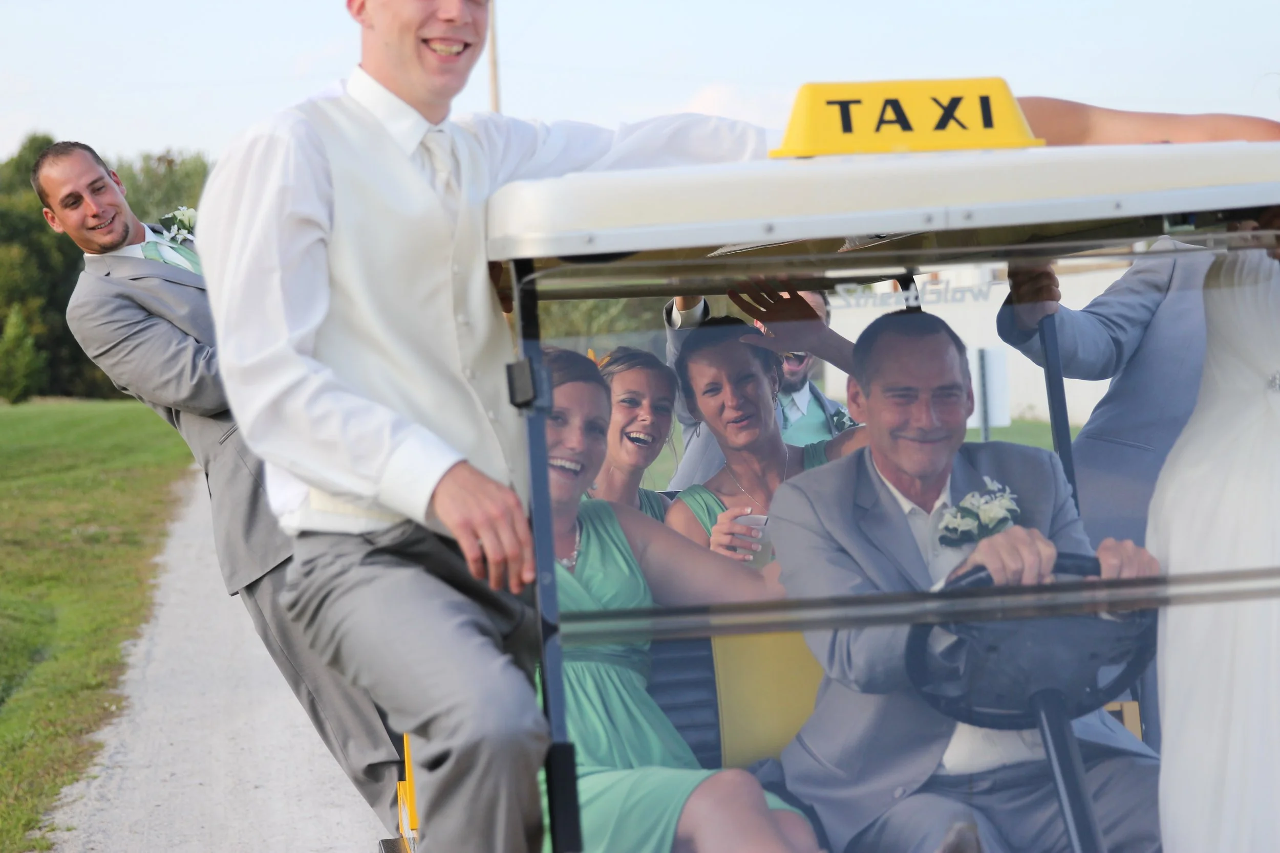 People riding in a golf cart on a golf course, with some of them dressed for a wedding celebration.