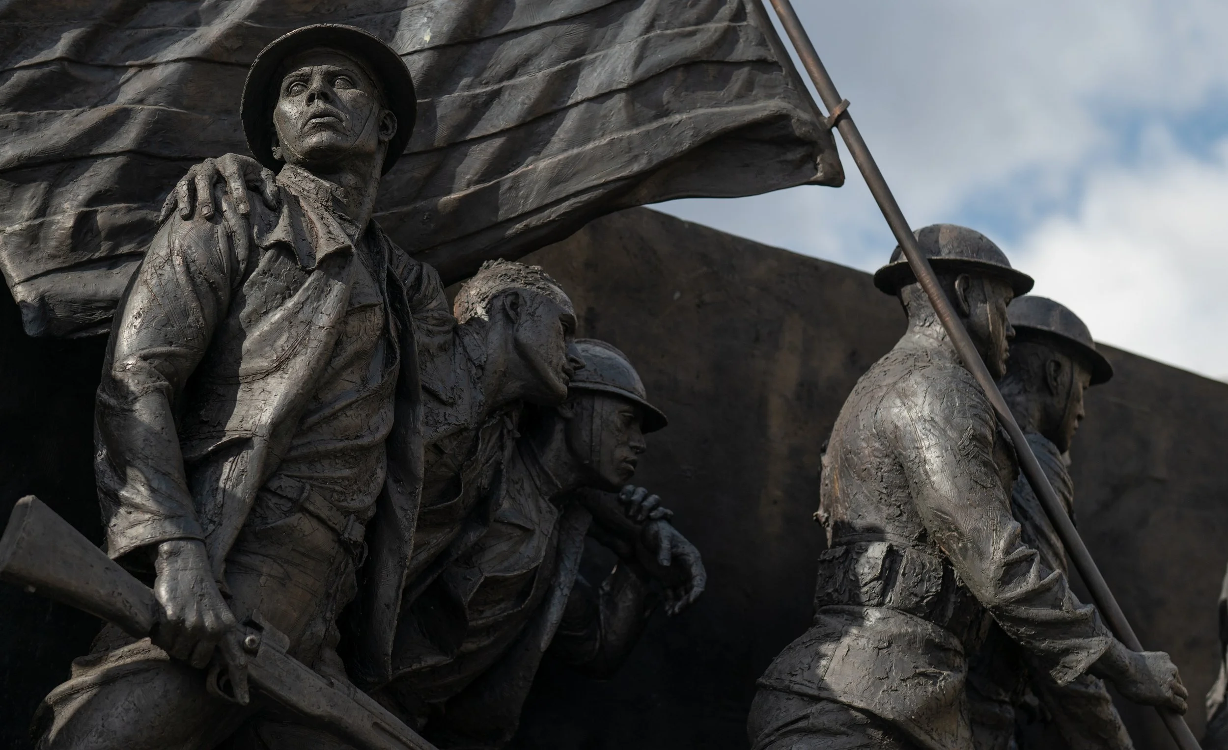 Close-up of the World War II memorial sculpture depicting soldiers in uniform with helmets, carrying weapons, and holding a flag.