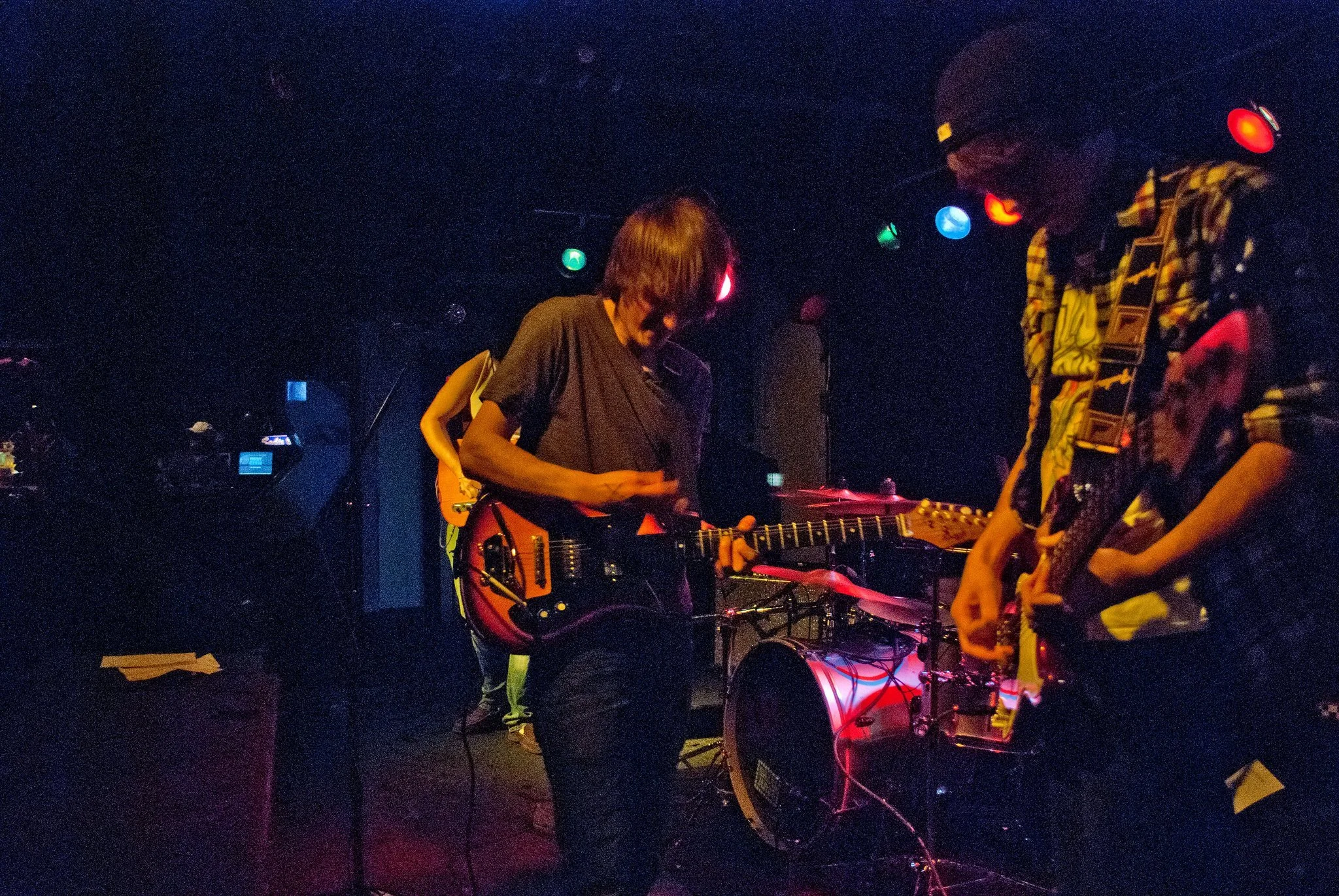 A band performing on stage with musicians playing electric guitars, in a dimly lit venue with colorful stage lights.