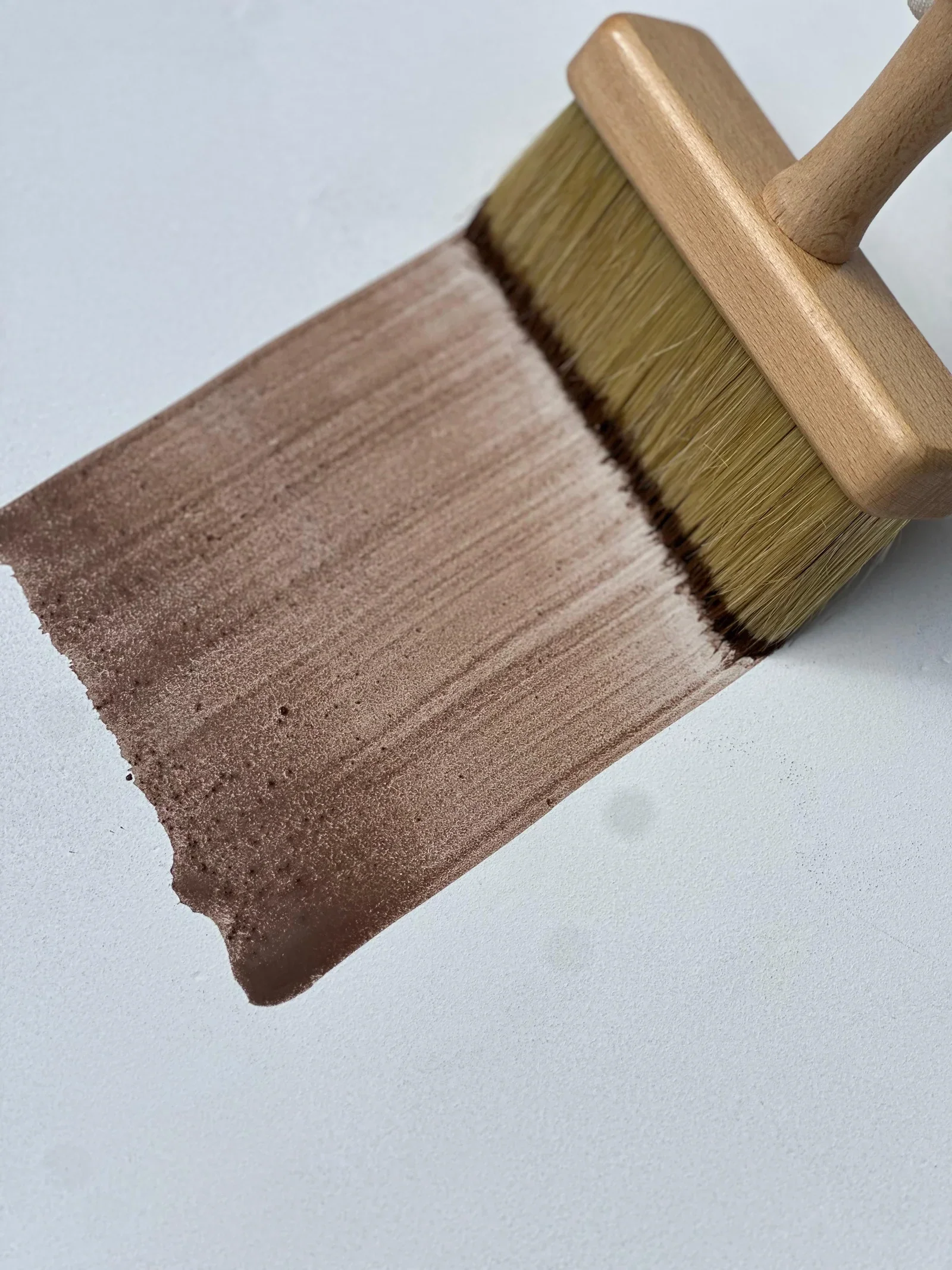Paintbrush with wooden handle and yellow bristles painted with brown paint on a white surface.