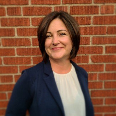 Sara smiling at you in front of a brick wall