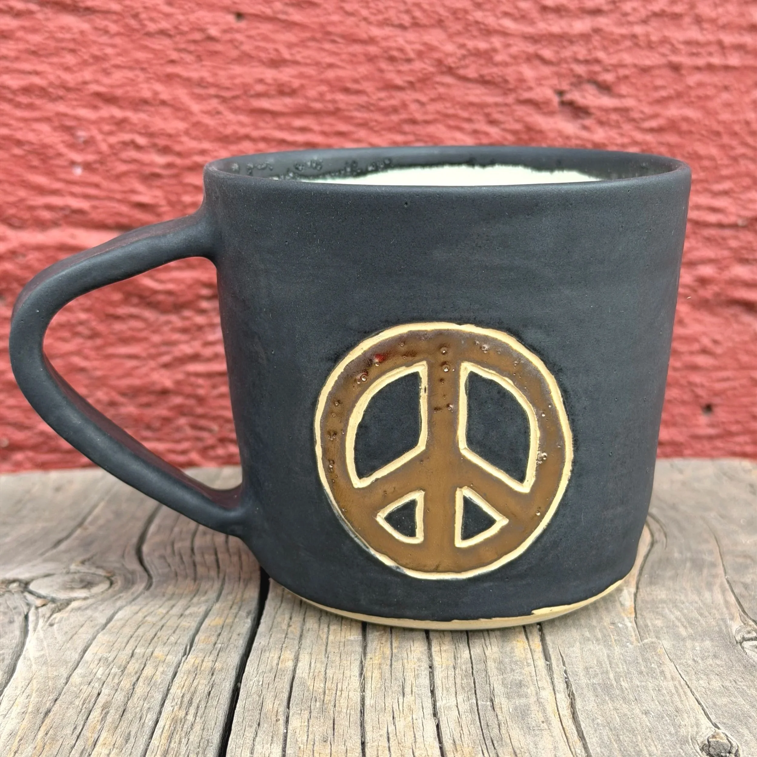 Handmade wheel thrown gold peace sign with black matte glaze on white clay mug modern design stoneware