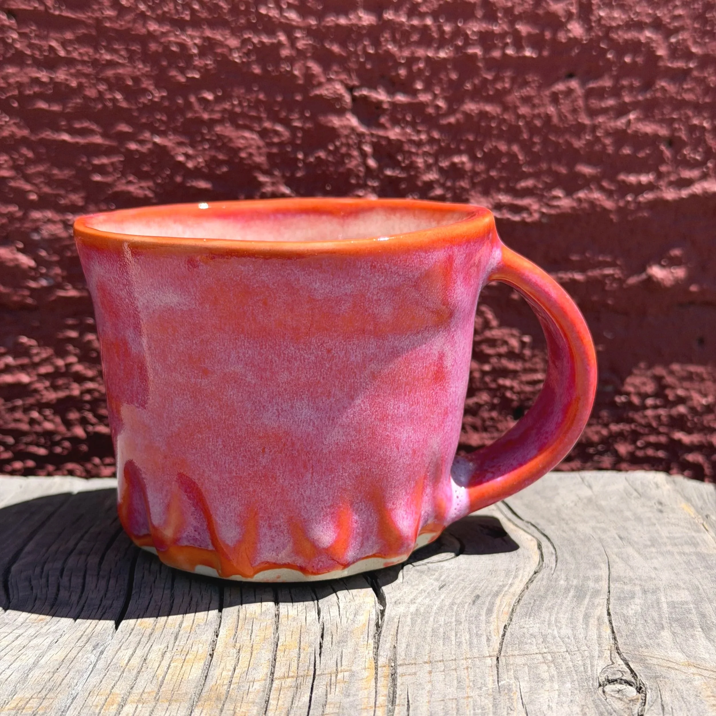 Bright red and orange glazes on a carved mug in white clay