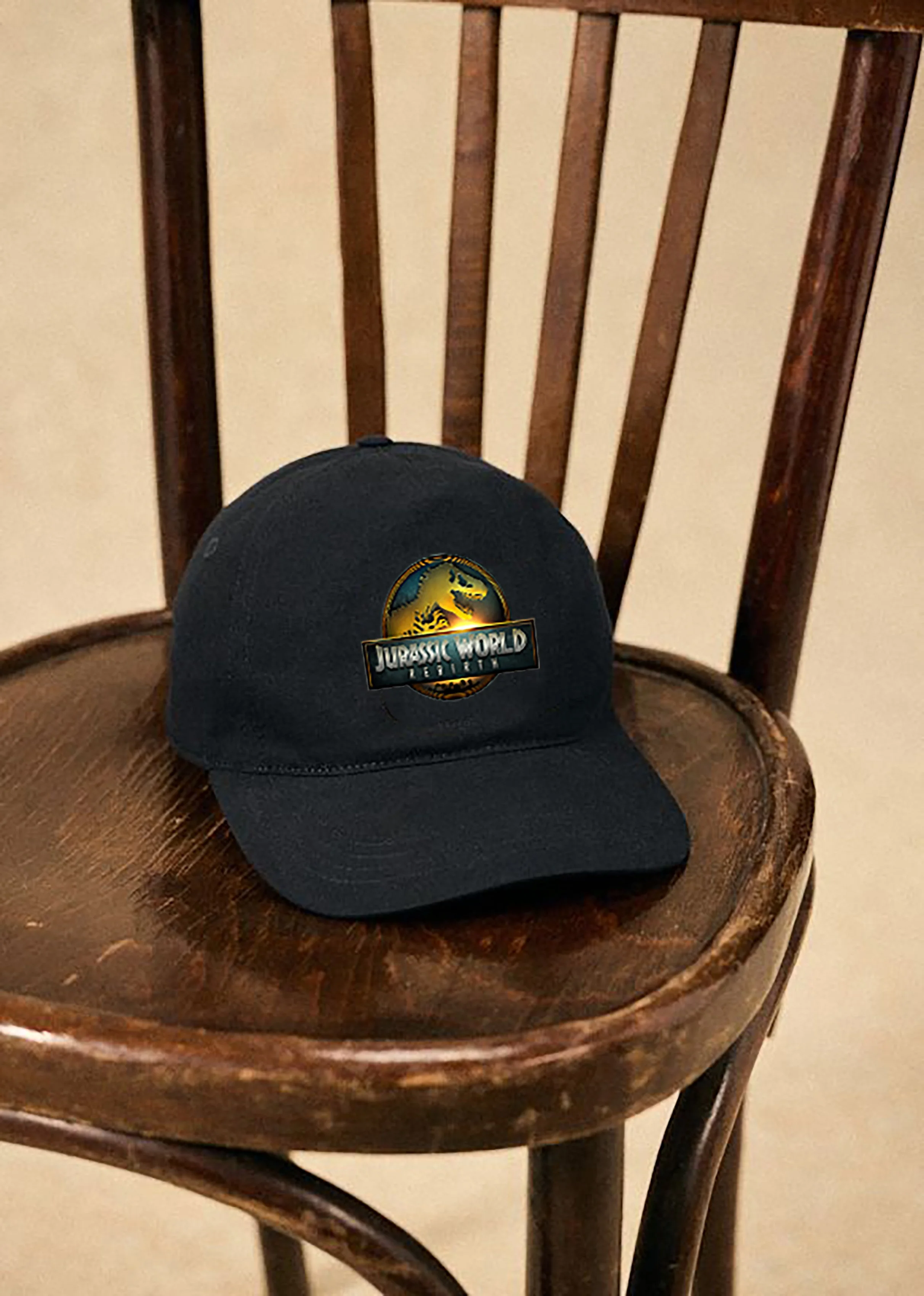 Black baseball cap with Jurassic World logo resting on a wooden chair.