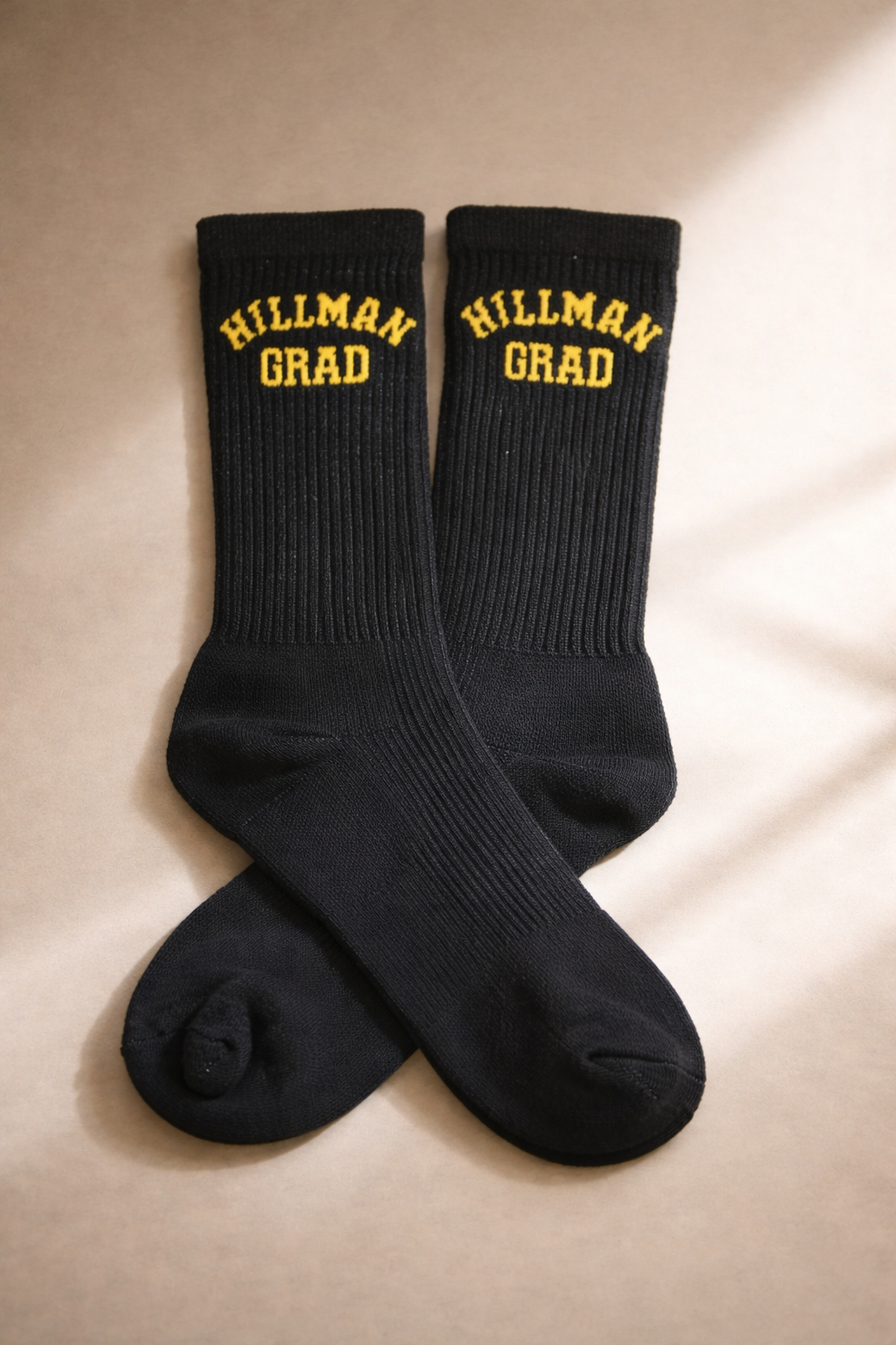 A pair of black crew socks with yellow embroidery reading "HILLMAN GRAD" on the top.