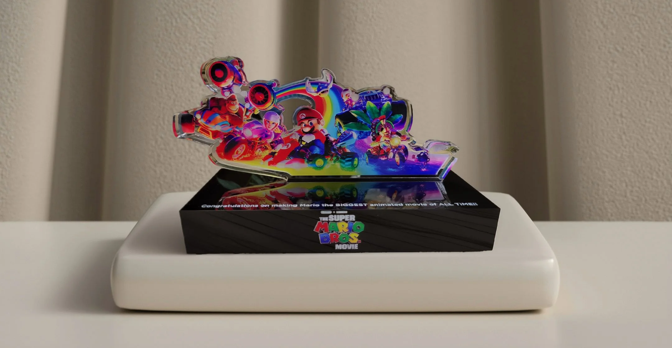 Colorful Super Mario Bros. promotional item featuring characters and scenes from the Mario video game franchise, displayed on a black base with a white platform.