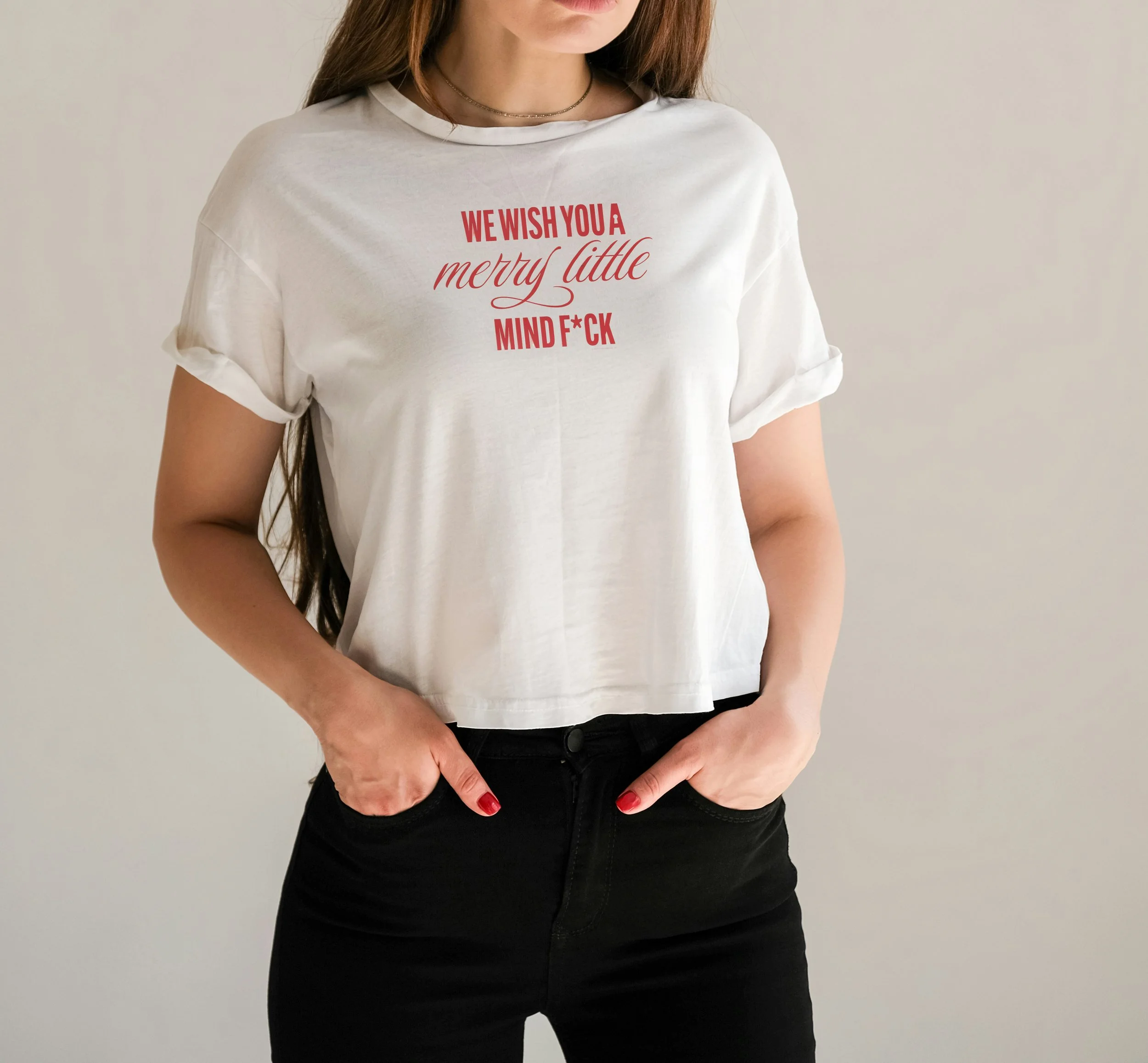 A woman wearing a white T-shirt with red text that reads 'WE WISH YOU A merry little MIND F*CK,' paired with black pants and red nail polish.
