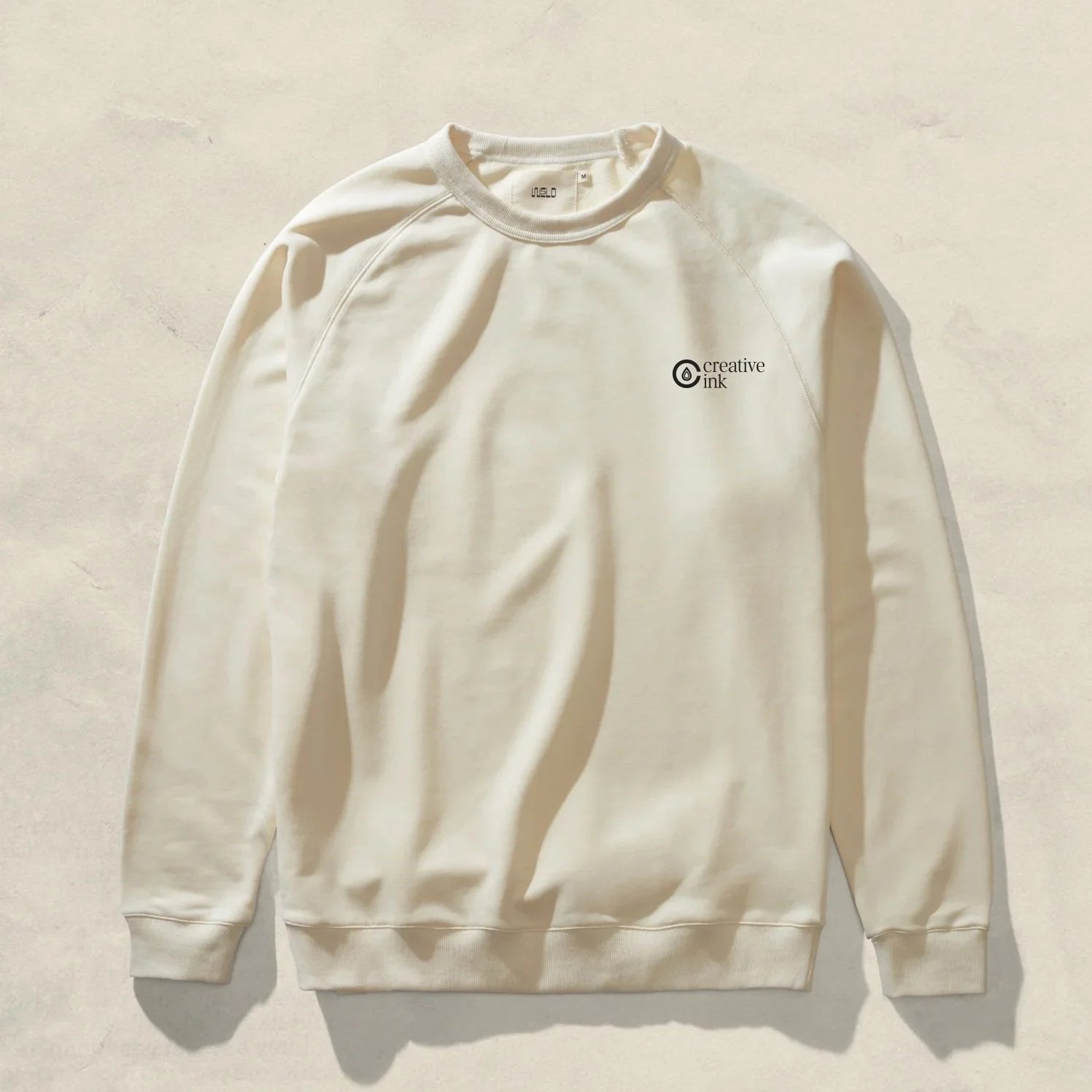 White crewneck sweatshirt with small 'Creative Ink' logo on left chest placed on a light-colored surface.