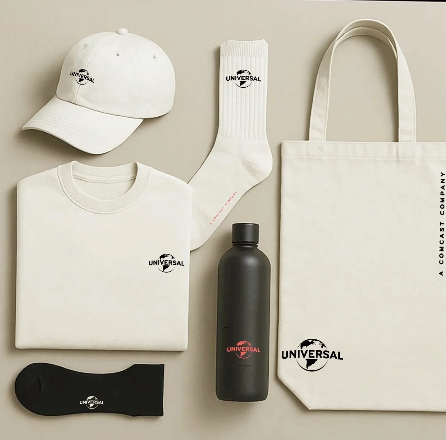 Collection of white and black promotional apparel and accessories, including a white baseball cap, white socks, white t-shirt, black water bottle, black sock, and beige tote bag, all branded with the Universal logo and text.