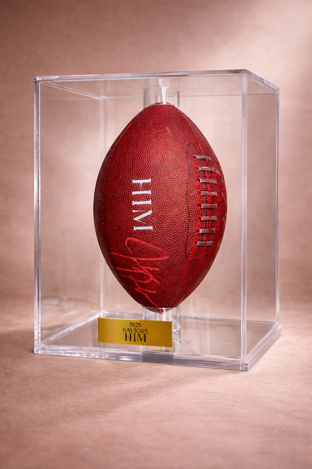 A red football encased in a clear display box with a gold plaque labeled '2025 Saviors HIM' at the base.
