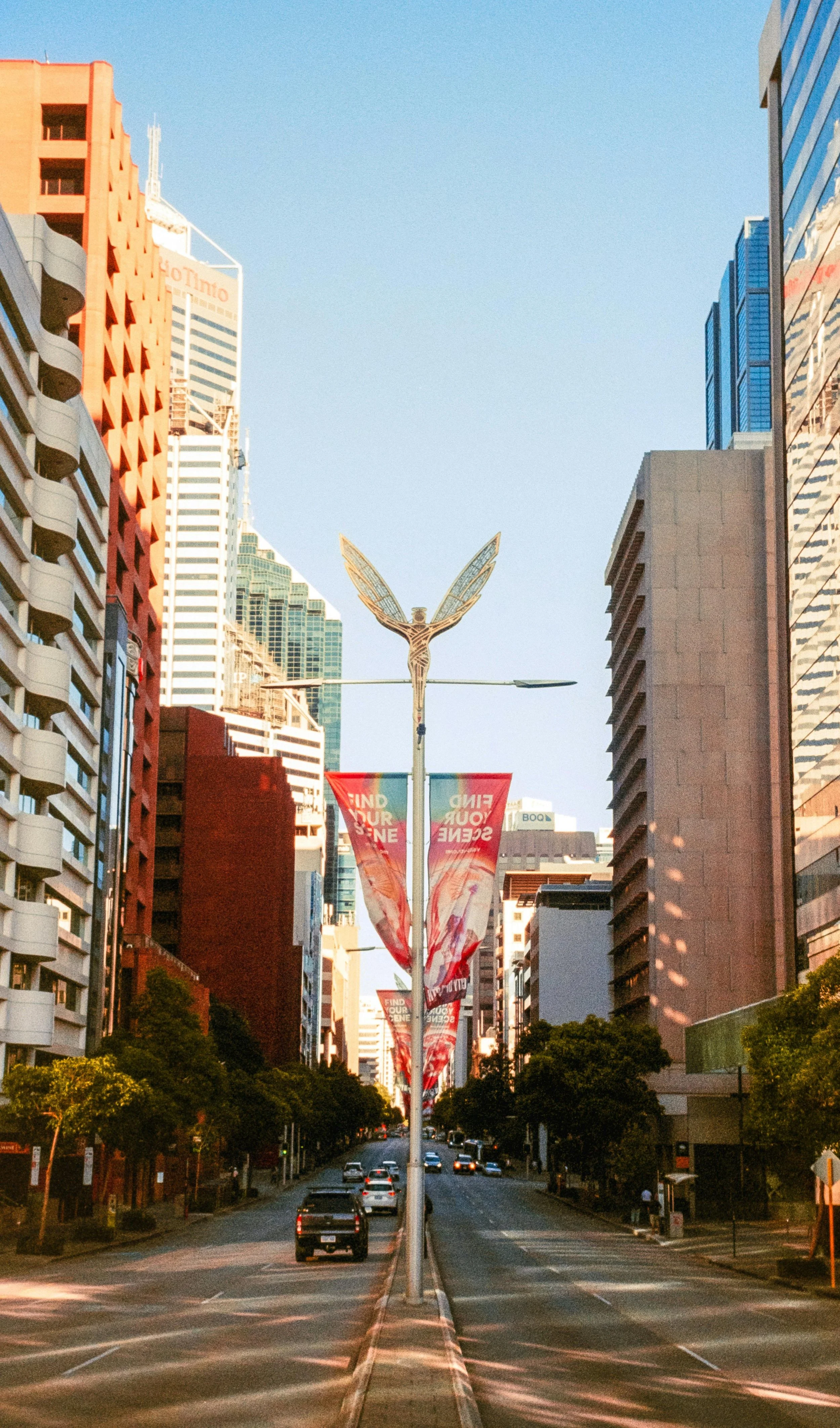 City street with tall buildings, banners, and a decorative streetlight with insect wings on top.
