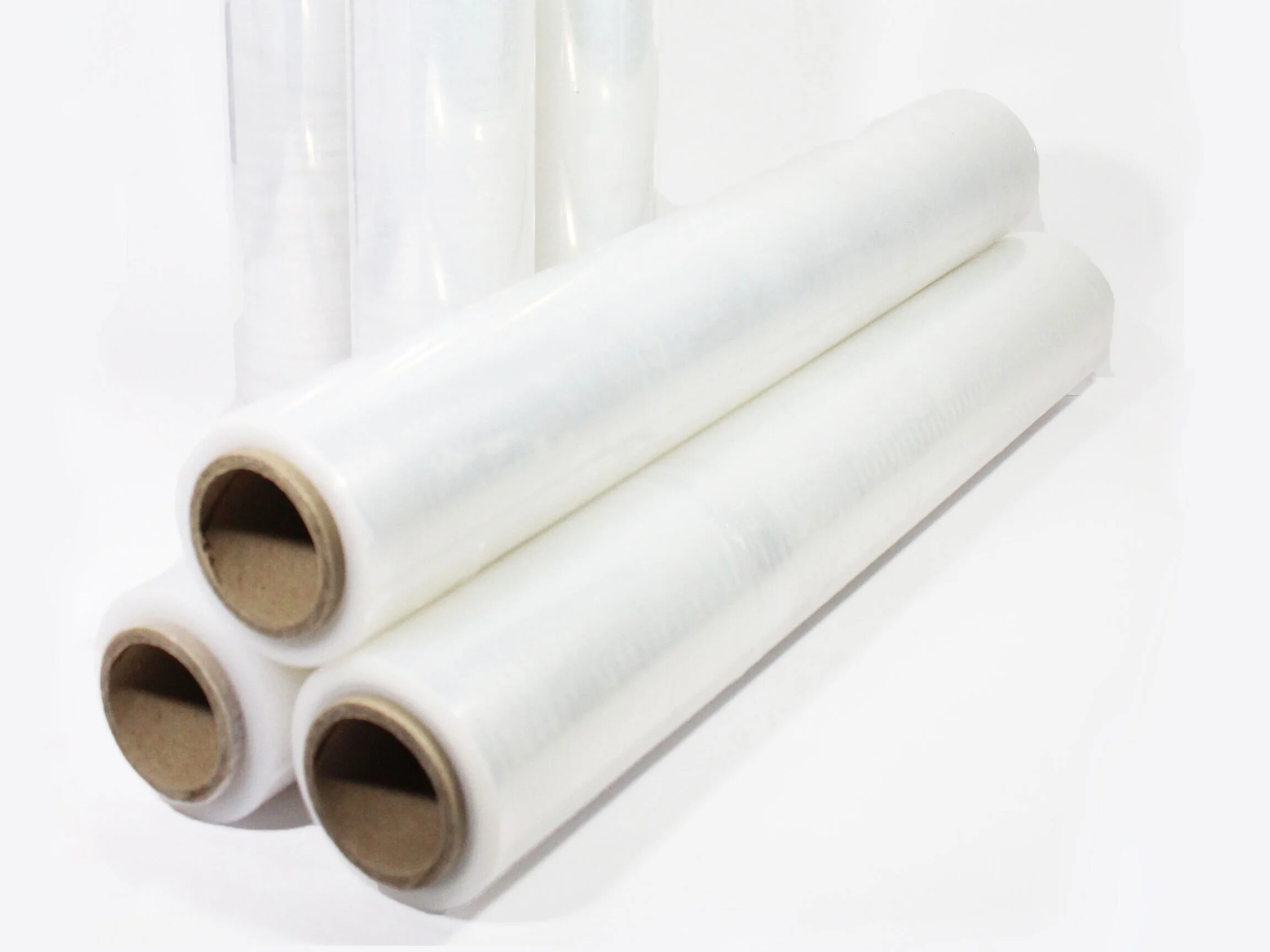 Three large rolls of clear plastic wrap lying on a white surface with additional rolls of plastic wrap standing upright in the background.