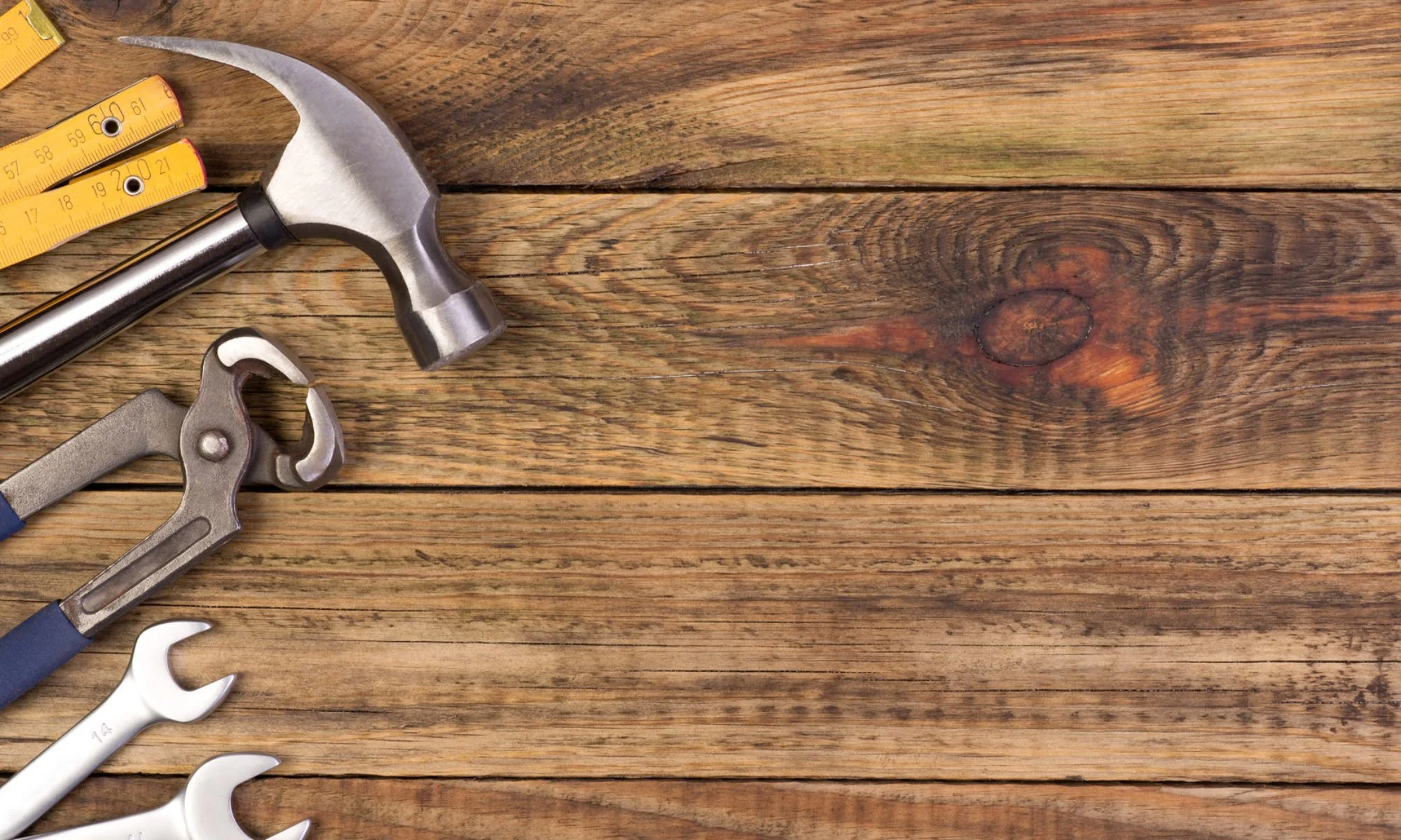 Hammer, adjustable wrench, and open-end wrenches on a wooden surface with a tape measure nearby.