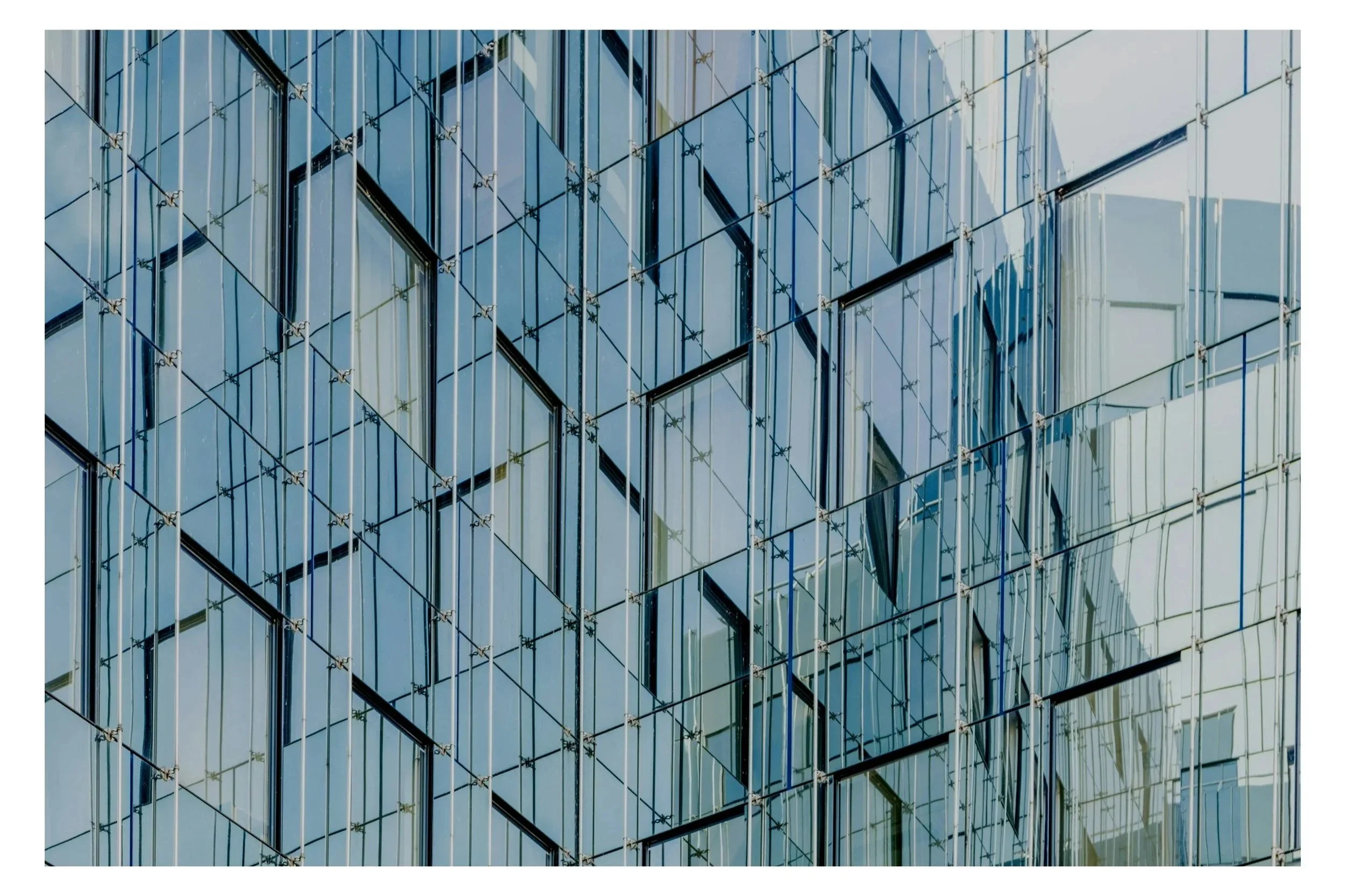 Close-up view of a modern glass building facade with reflective windows and metal framing, creating geometric patterns.
